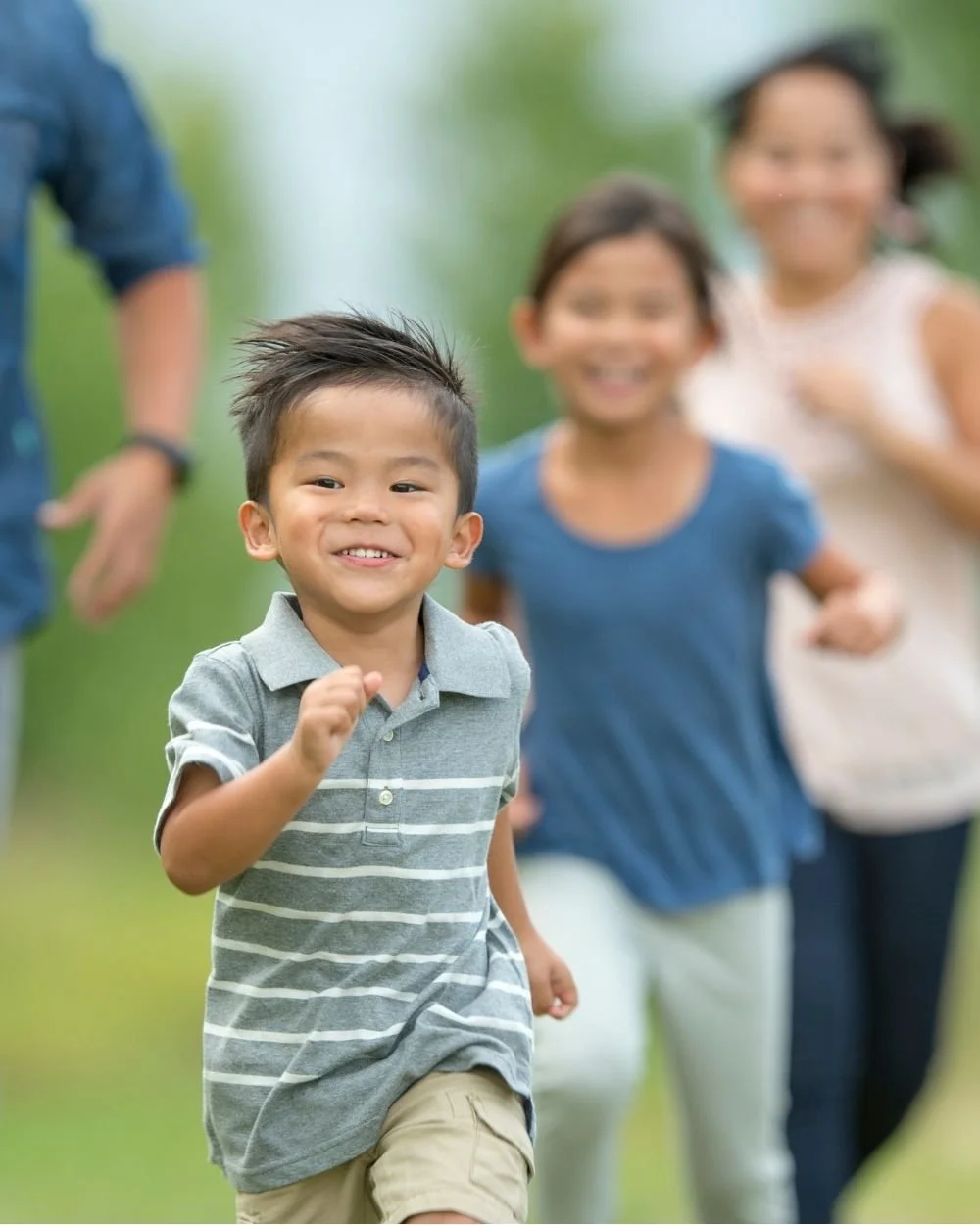 A young boy running outdoors with a smile, followed by two women and one man.