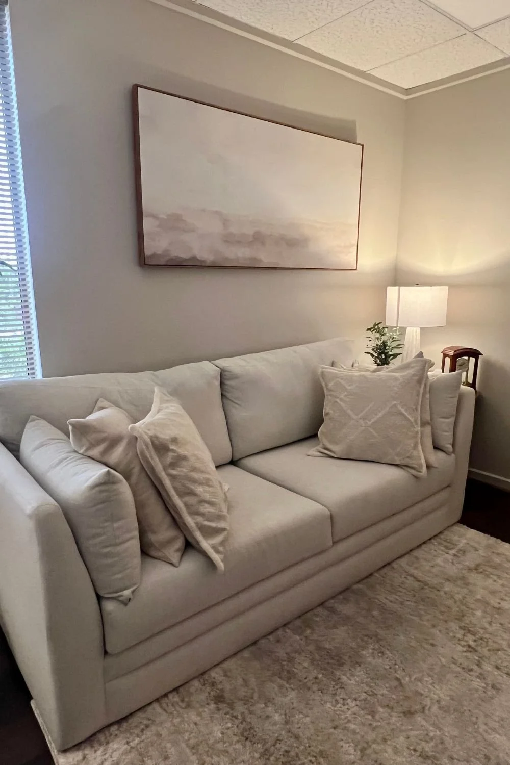 Therapy office with multiple white pillows on a couch with a framed abstract art piece above it.