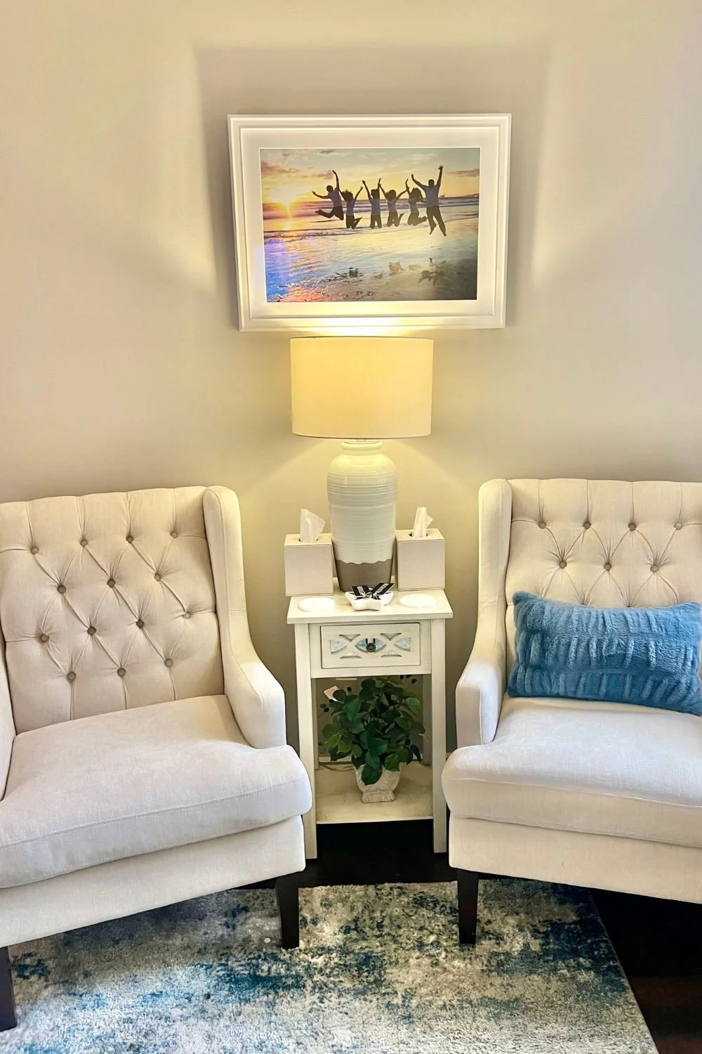 A cozy therapy office with two cream armchairs and a small white side table with a plant underneath.