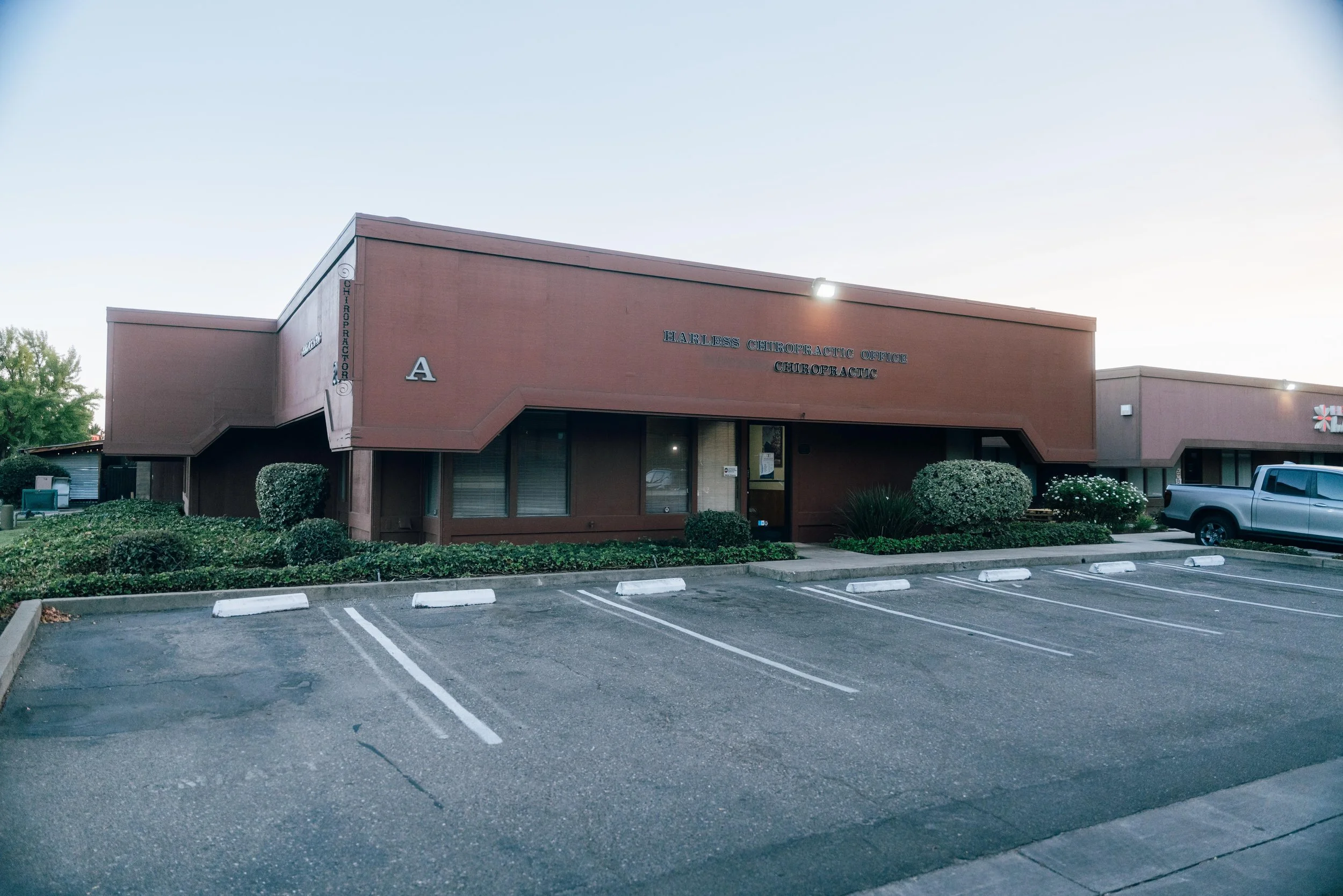 Parking lot in front of a chiropractic office building with empty parking spaces and bushes.