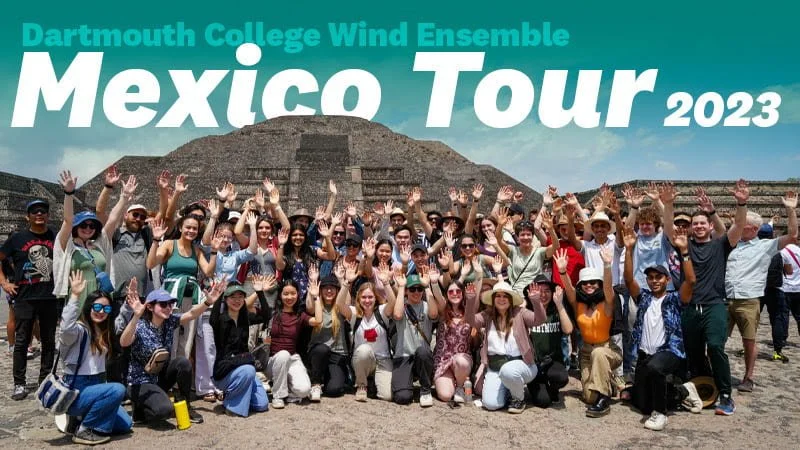 Large group of people posing for a photo in front of a pyramid at Chichen Itza in Mexico. They are waving at the camera and smiling, with the text 'Dartmouth College Wind Ensemble Mexico Tour 2023' in the background.