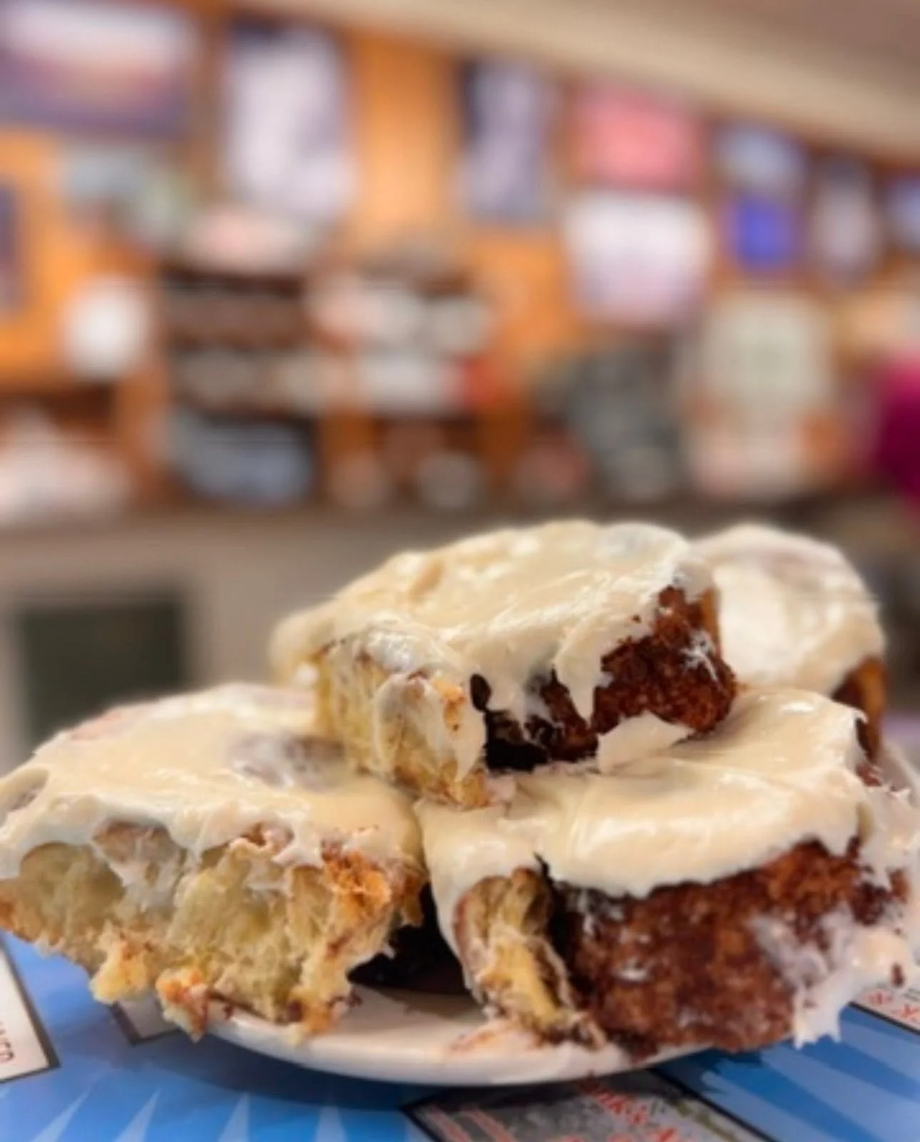 Close-up of a slice of chocolate cake with vanilla icing on a plate, with a blurred bookshelf in the background.