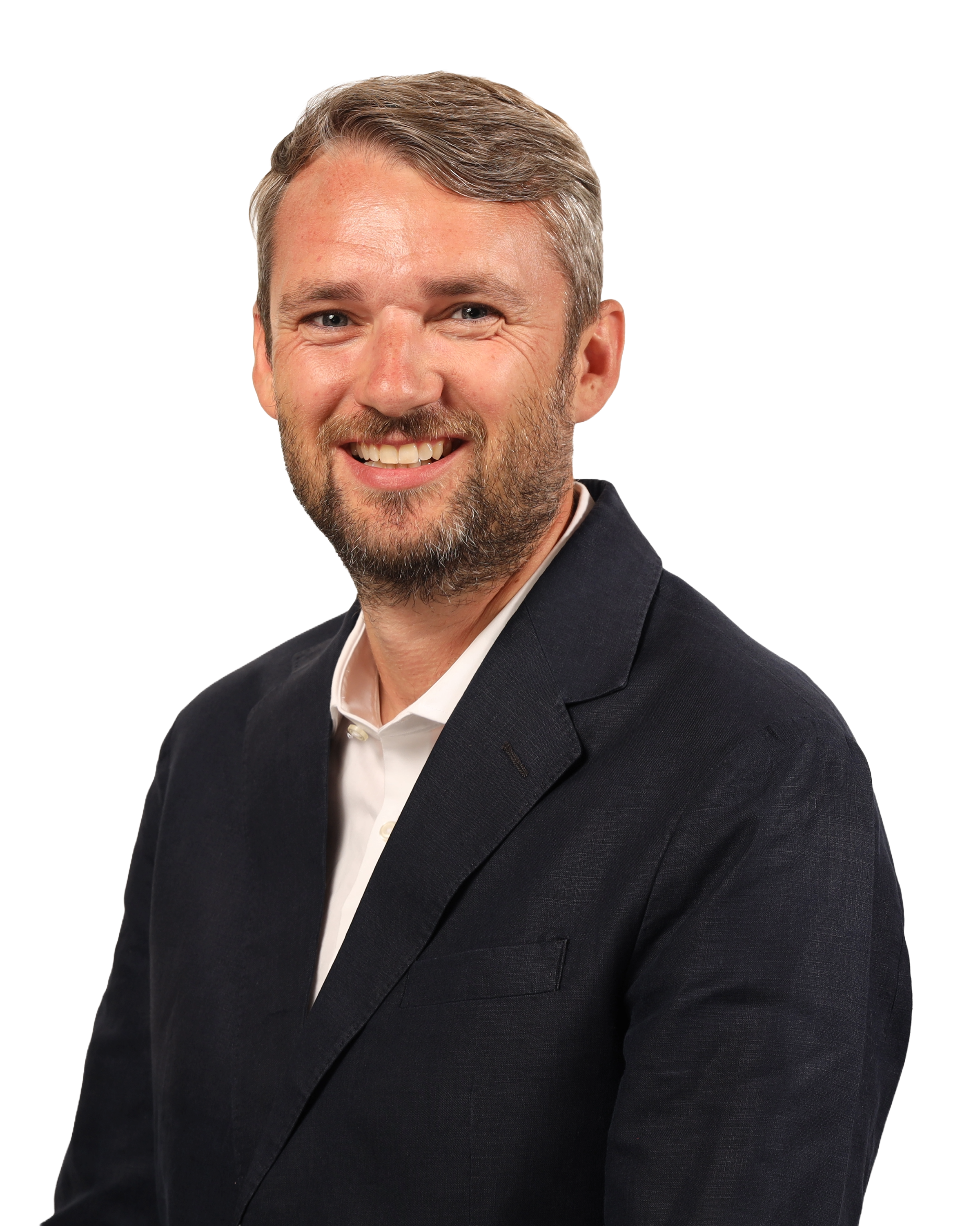 Portrait of a smiling man with a beard and short hair, wearing a dark suit and white shirt, against a black and white background.