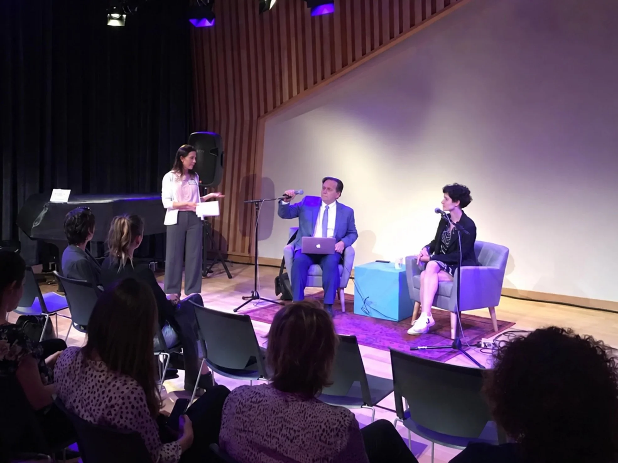 Woman moderates conversation between panelists on stage in front of a studio audience