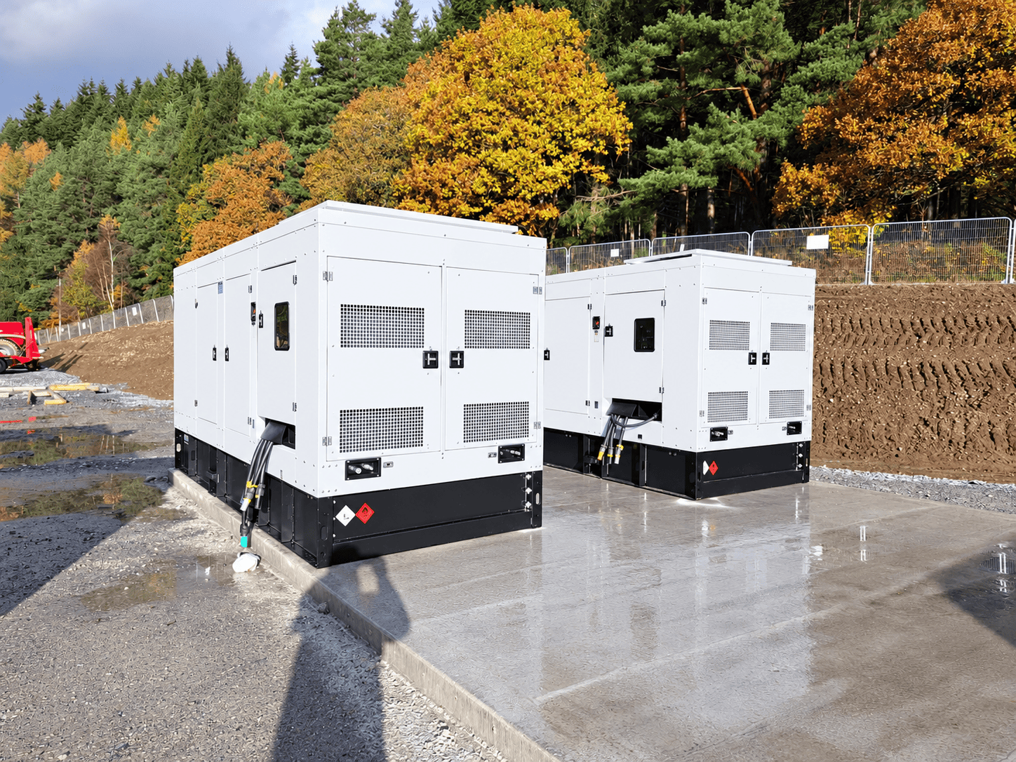 Two industrial generators installed on a concrete pad beside autumn woodland