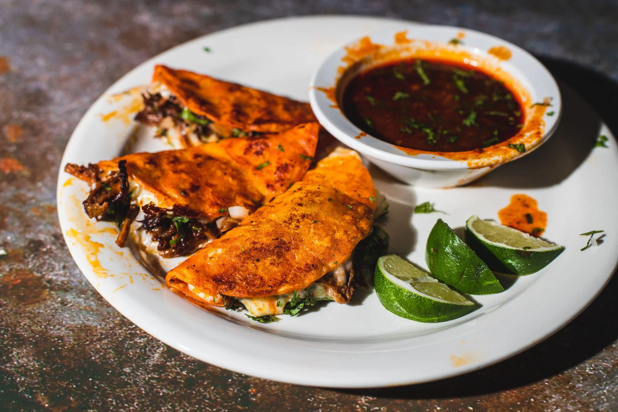 Plate of Mexican food with tacos filled with meat and vegetables, served with lime wedges and a bowl of dark salsa.