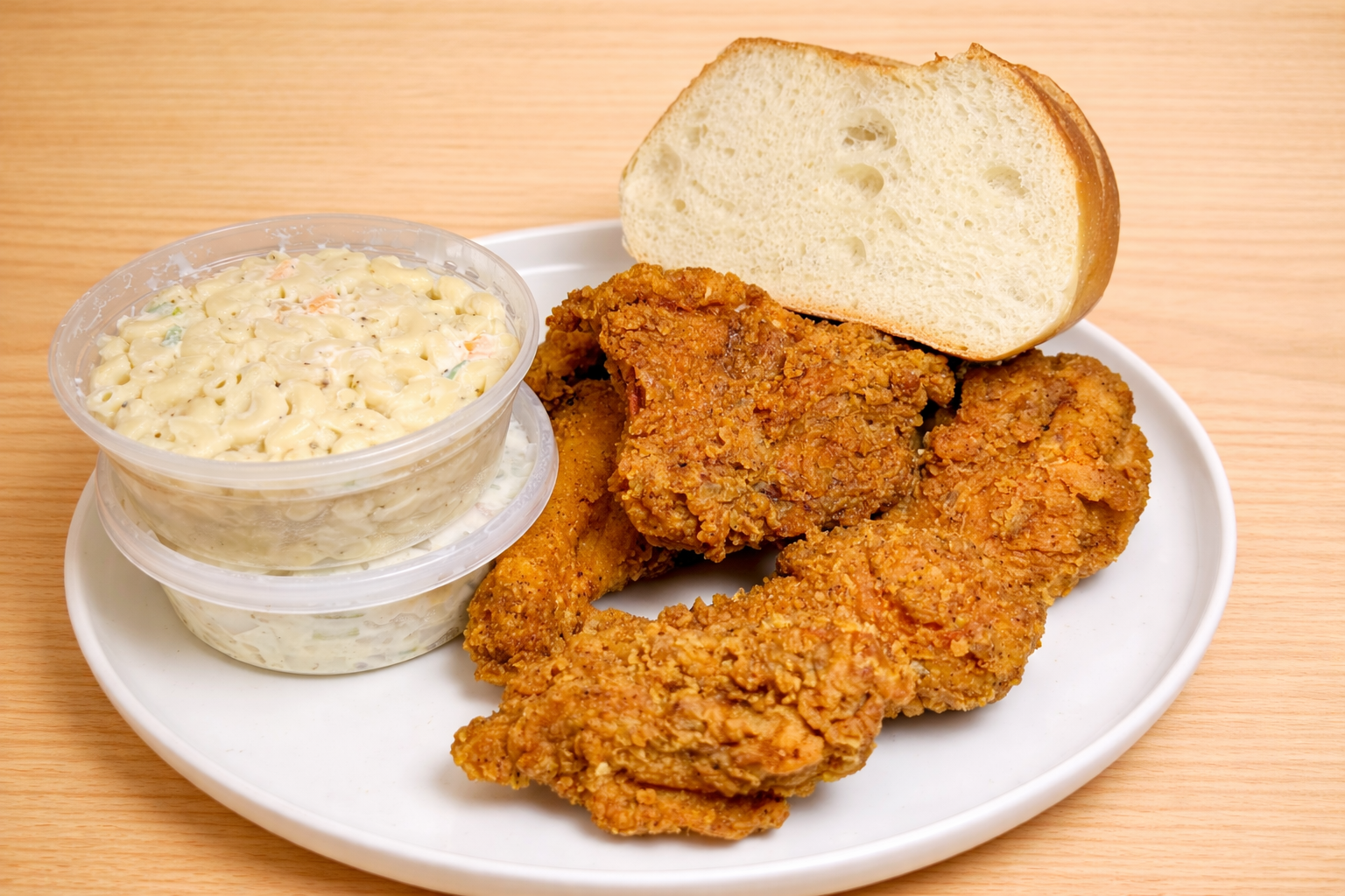 Fried chicken drumsticks and thighs with a slice of bread, served with a side of macaroni salad on a white plate