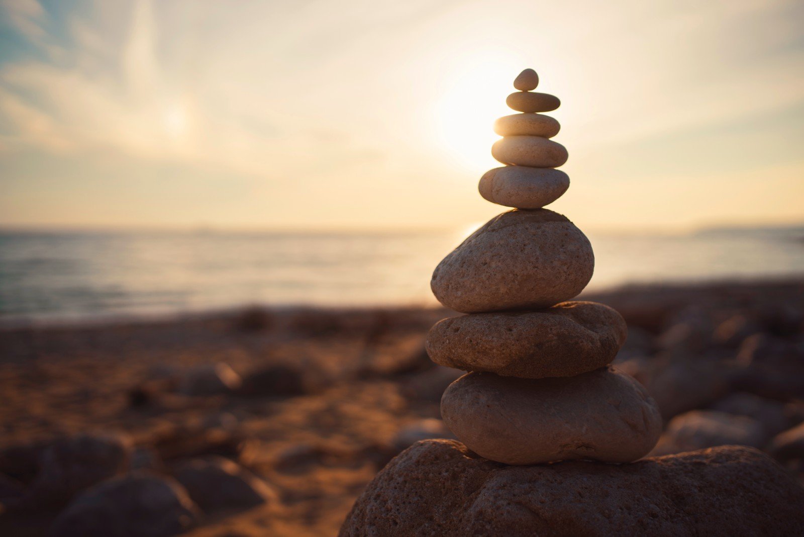 Stacked rocks on a rocky beach with ocean and blue sky in the background.
