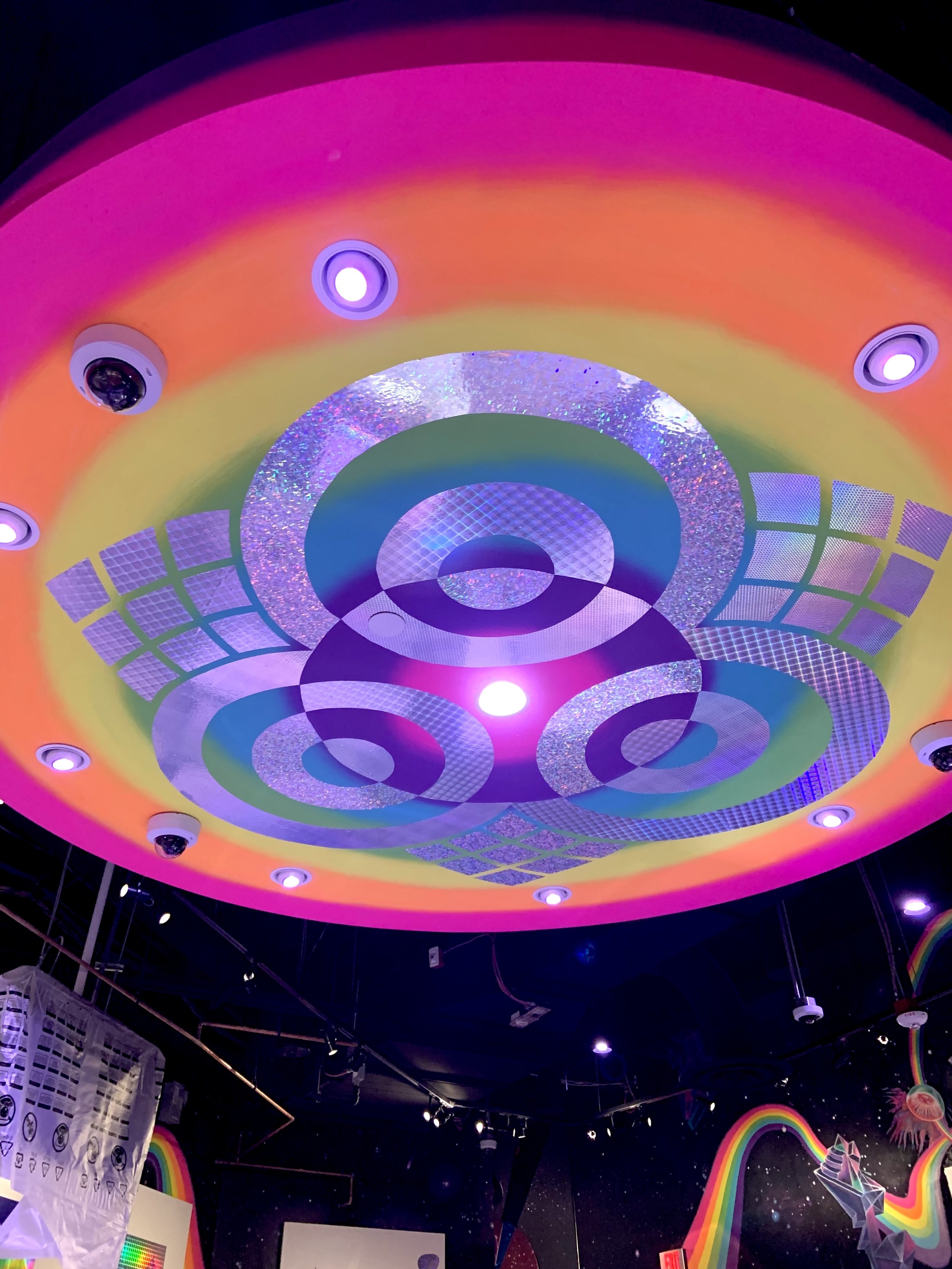 Colorful ceiling with a rainbow gradient border, circular lights, and abstract geometric patterns in bright colors and metallic textures.