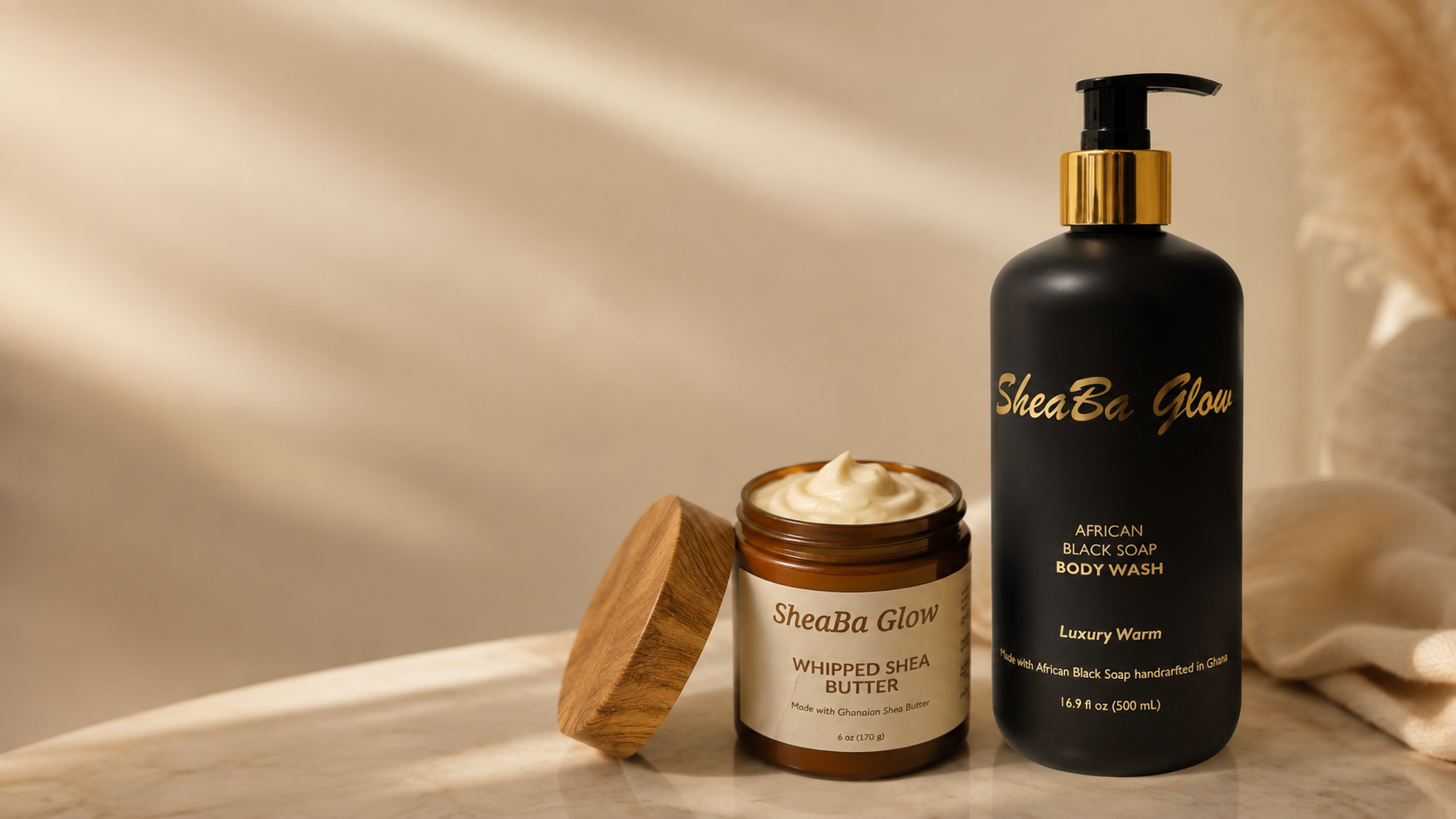 A black pump bottle labeled SheaBa Glow African Black Soap Body Wash and a jar of SheaBa Glow Whipped Shea Butter with a wooden lid on a marble surface with a light-colored blurred background.