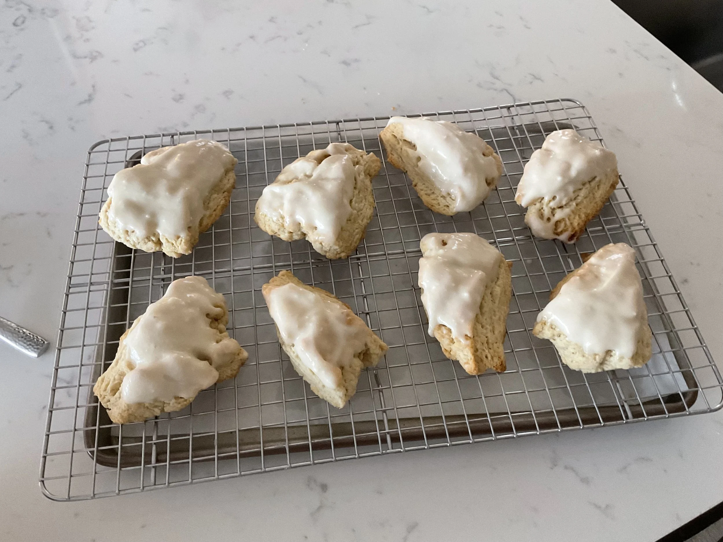 Four partially frosted scones on a cooling rack placed on a white marble countertop.