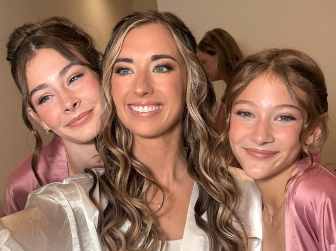A woman and two young girls taking a selfie together, all smiling, with the women in the center and the girls on either side, wearing satin pink robes.