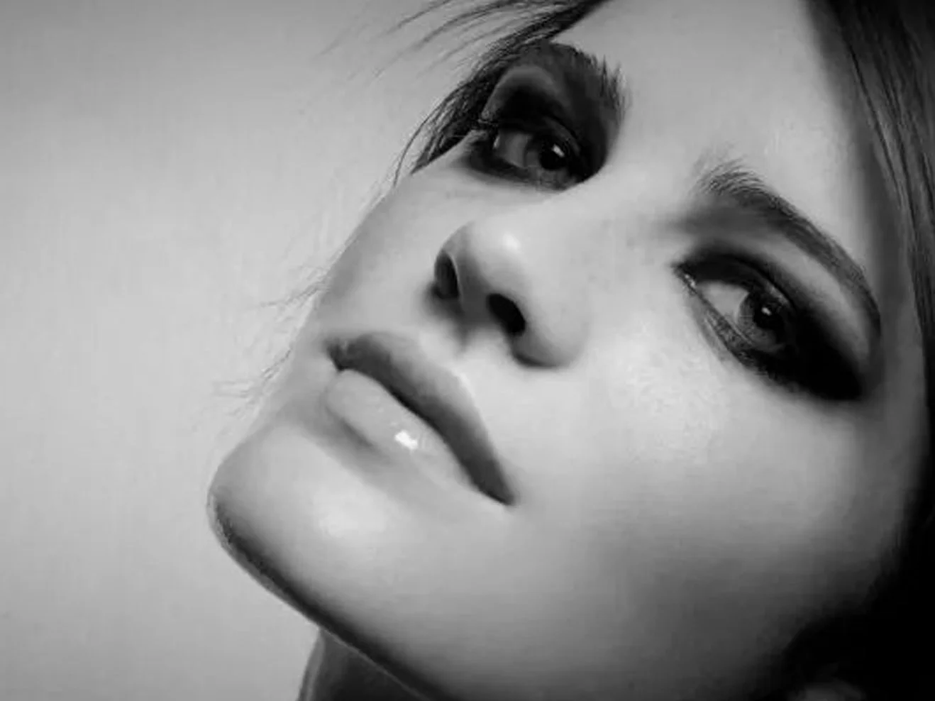 Close-up black and white photo of a woman looking at the camera with a pensive expression, with makeup emphasizing her eyes.