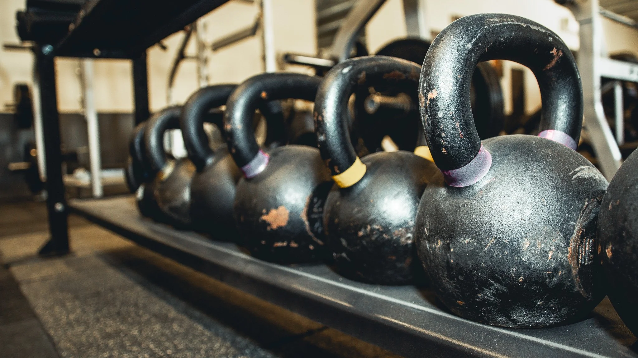 A row of black kettlebells on a gym rack, showing signs of wear and rust.