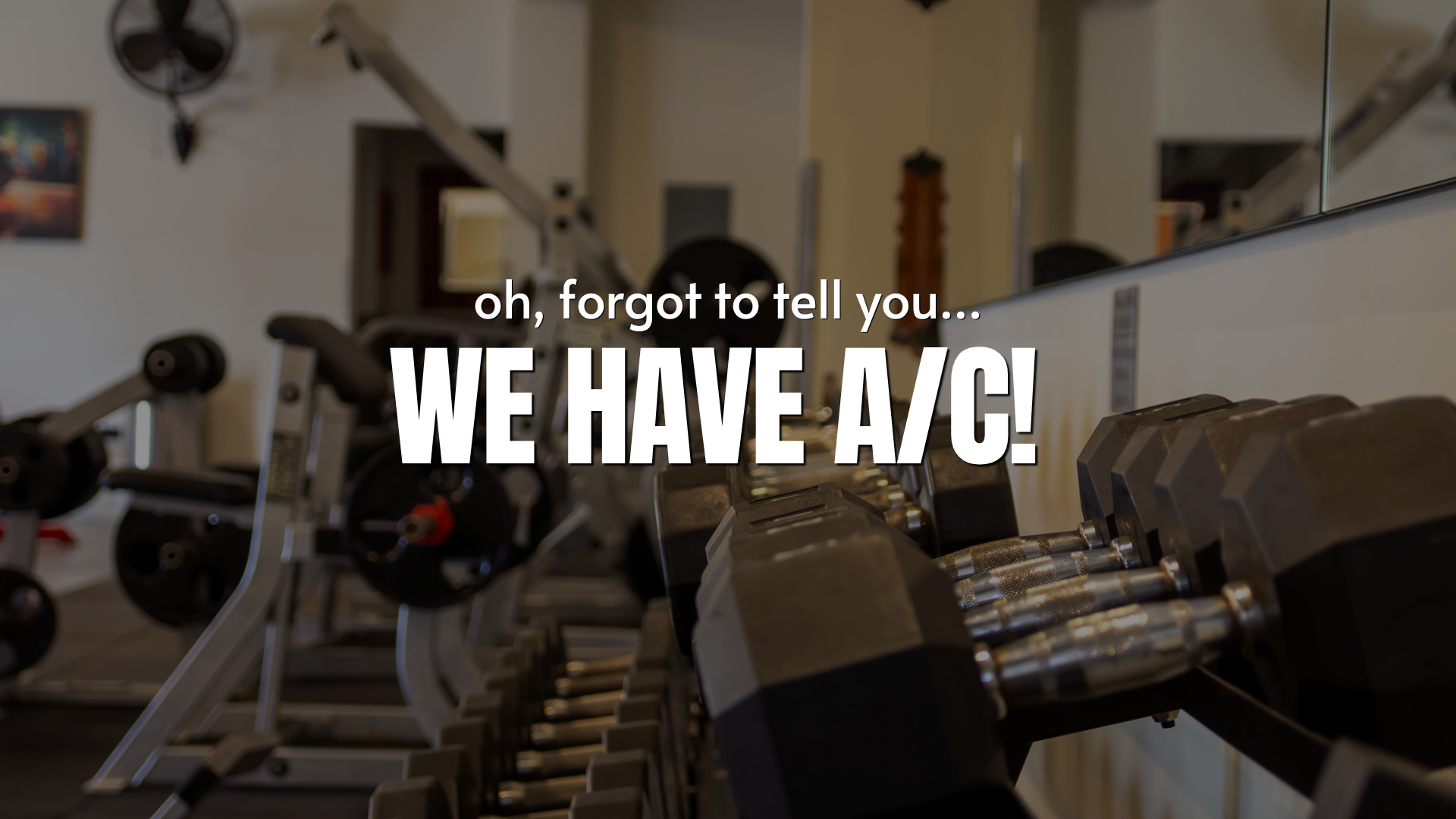 Gym equipment including dumbbells and weight machines with overlaid text that says, 'oh, forgot to tell you... WE HAVE A/C!'