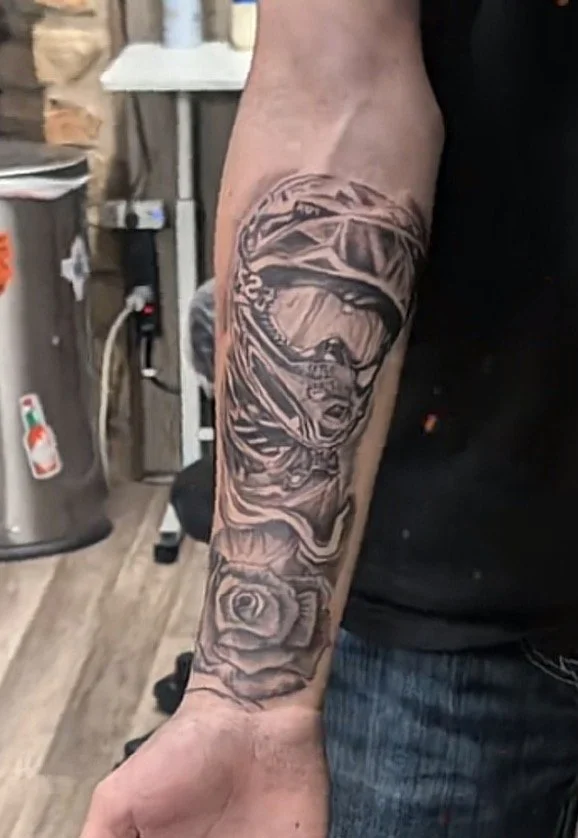 Tattoo of a woman wearing a helmet and veil, with a rose at the bottom, on a person's forearm.