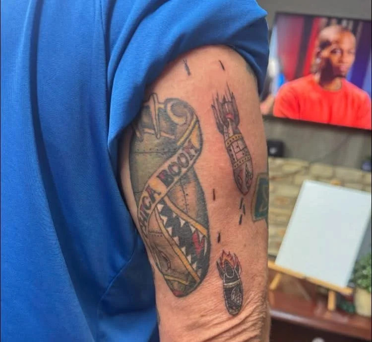 Tattoo of a large fish with an open mouth, sharp teeth, and a banner reading "Kick Ass," on a person's upper arm.