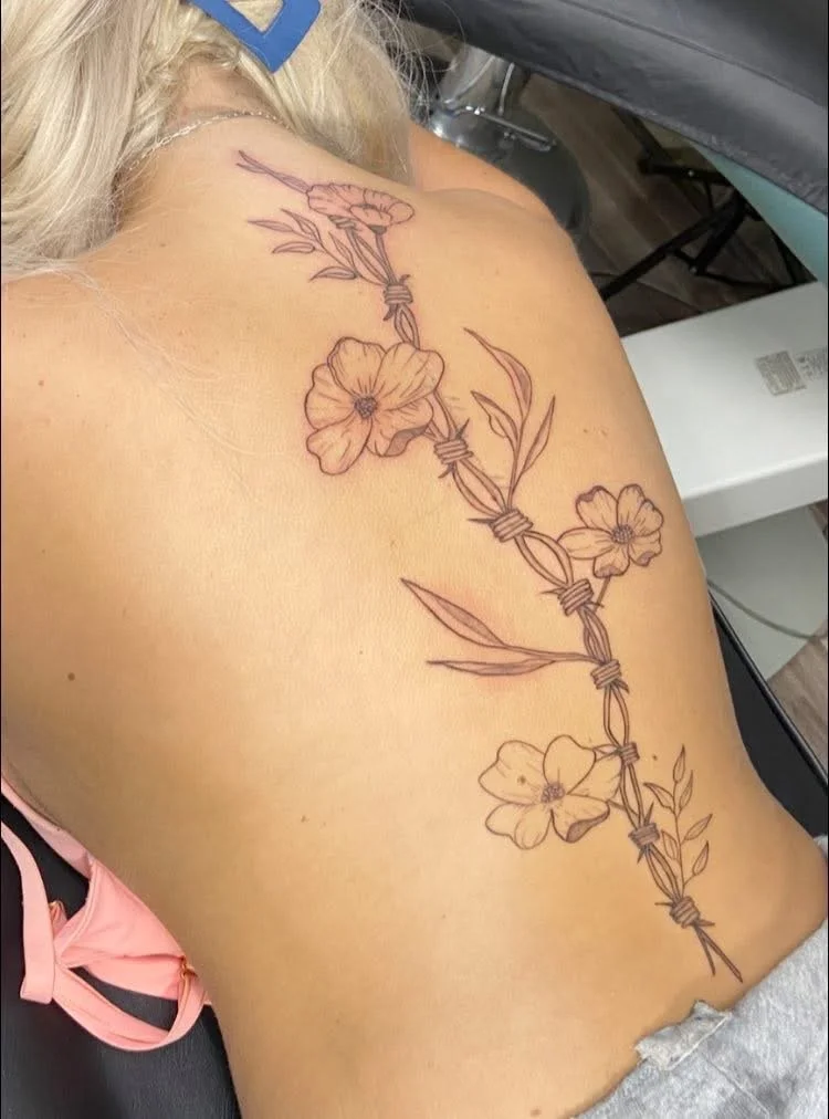 Tattoo of a barbed wire with flowers on a person's back.