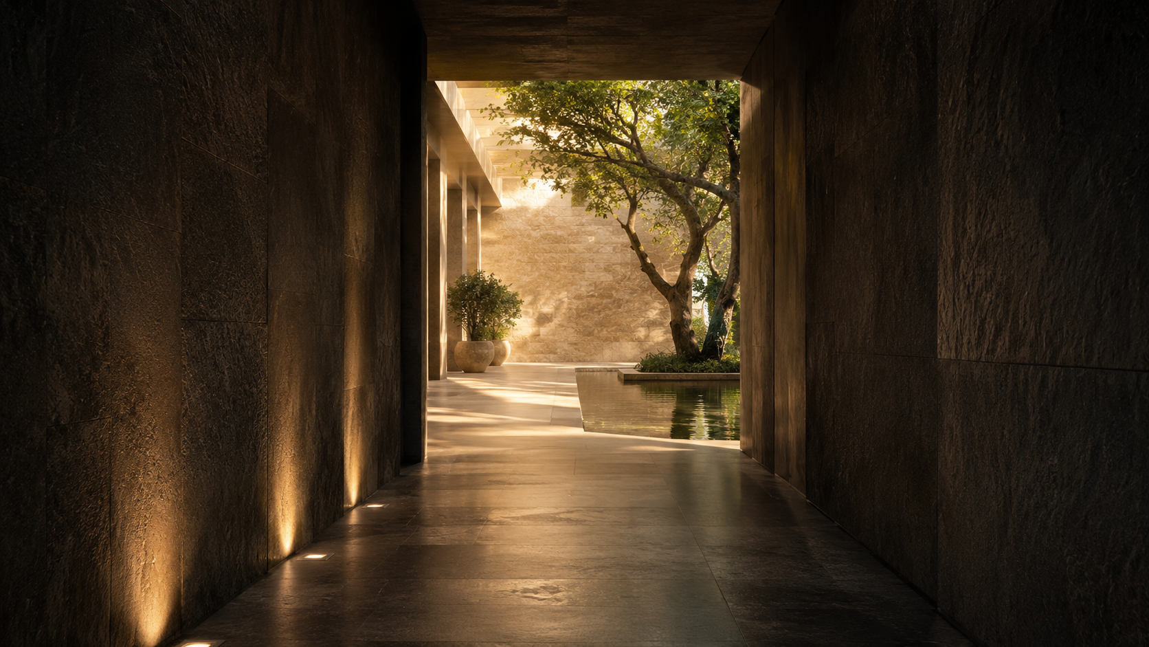 View from a dark, shaded corridor opening to a sunlit courtyard with a tree, potted plants, and a water feature.