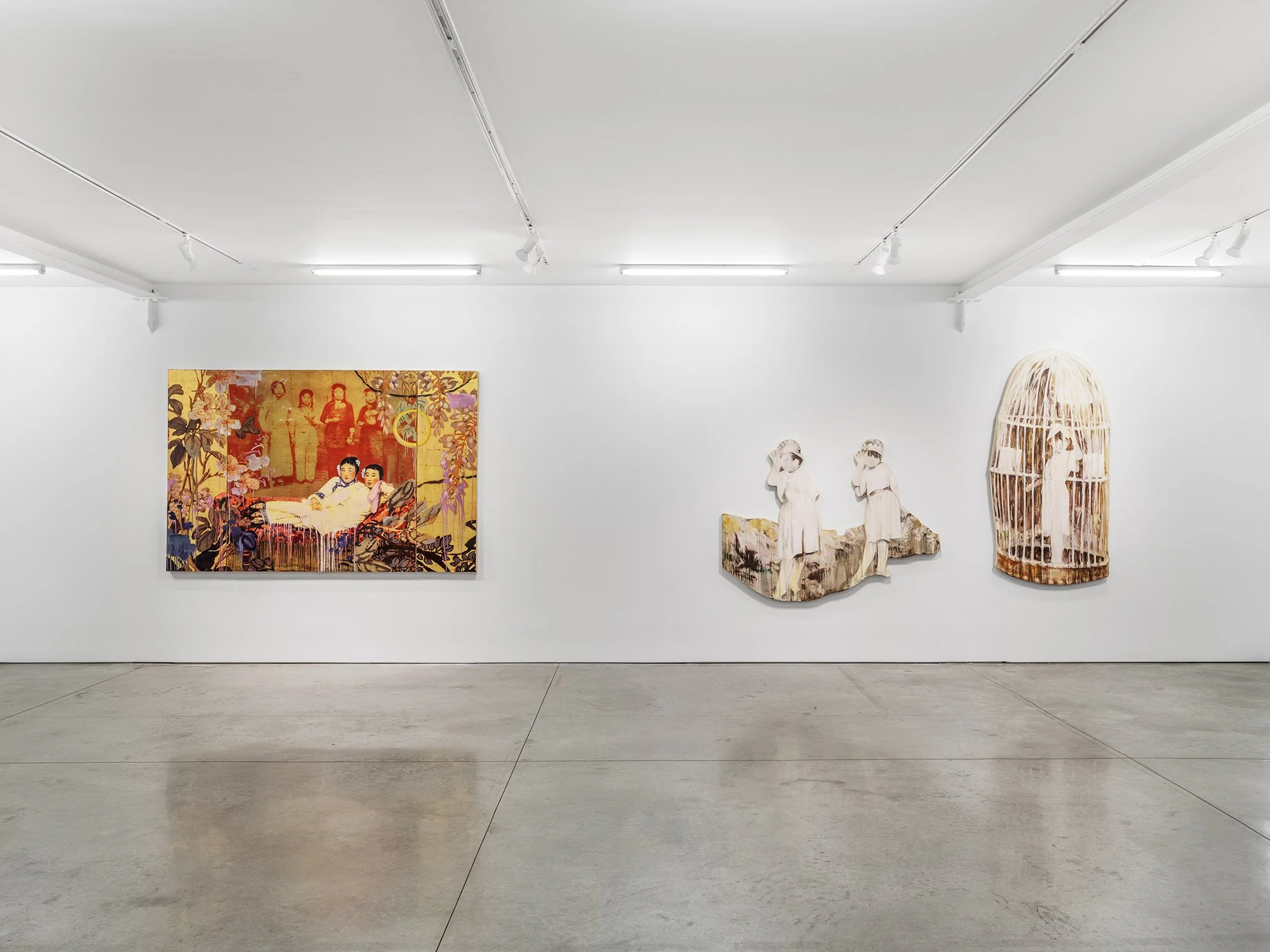 Art gallery display with a large colorful painting featuring women in traditional clothing and a series of smaller sculptures resembling children in white outfits, and a large bamboo-style art piece on the right.