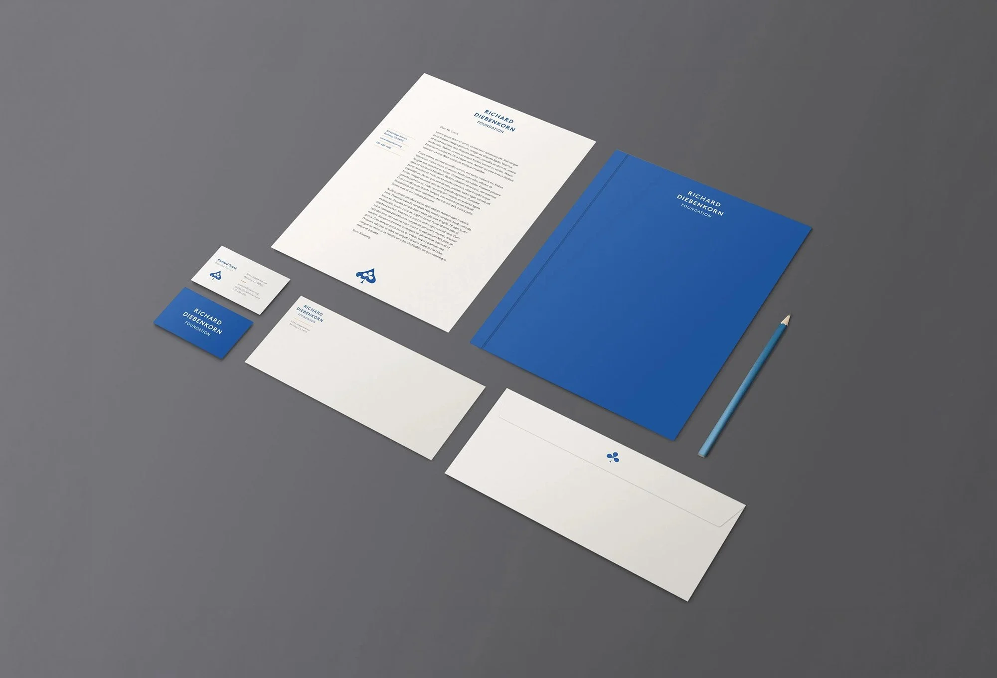 A letter, two business cards, a closed blue folder, and a blue pen are arranged on a gray surface, all branded with the Richard Diebenkorn Foundation logo and colors.