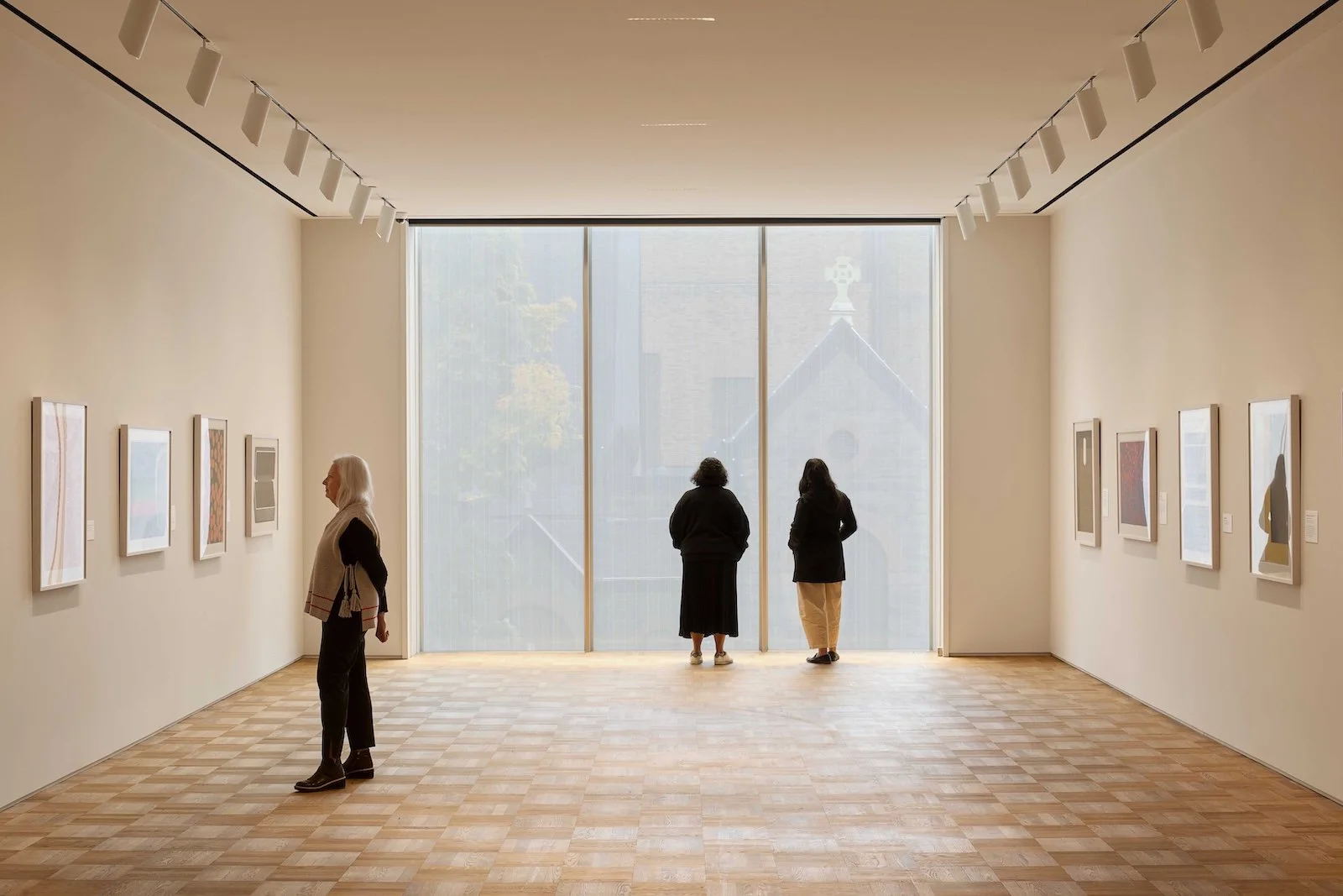 People viewing artwork in a modern art gallery with large window and wood flooring.