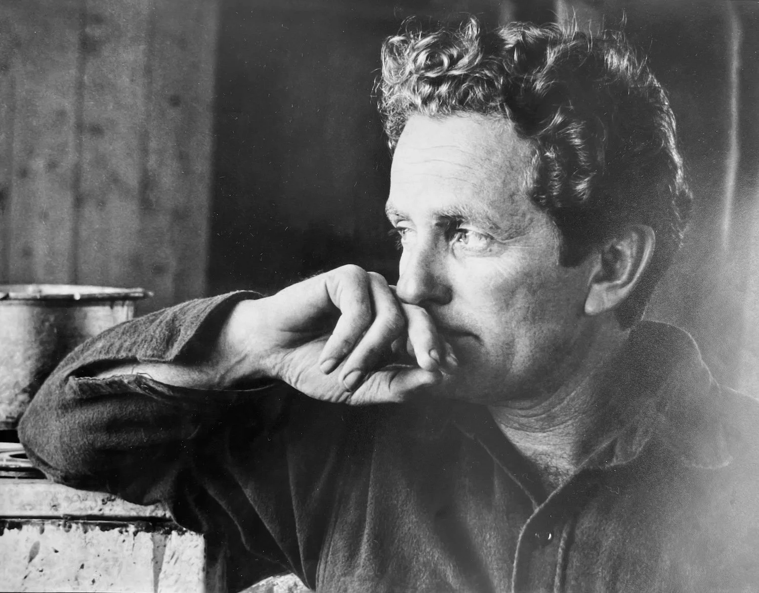 Black and white photograph of a woman with curly hair resting her chin on her hand, looking thoughtfully to the side.