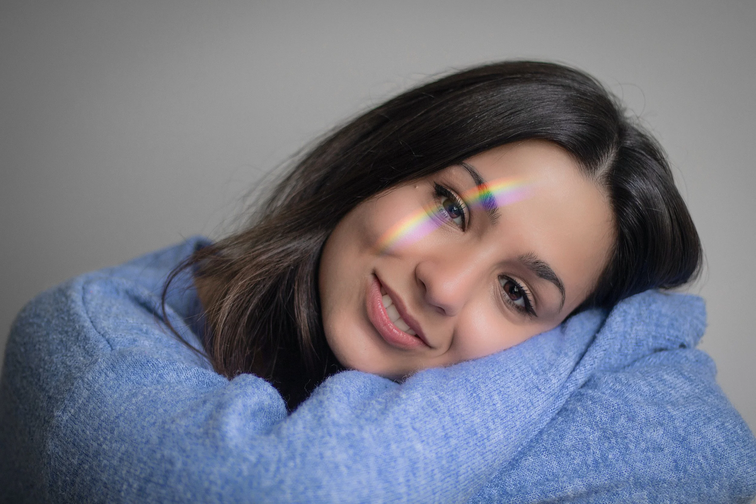 A woman laying her head down on her crossed arms with a rainbow of light shining across her eye.