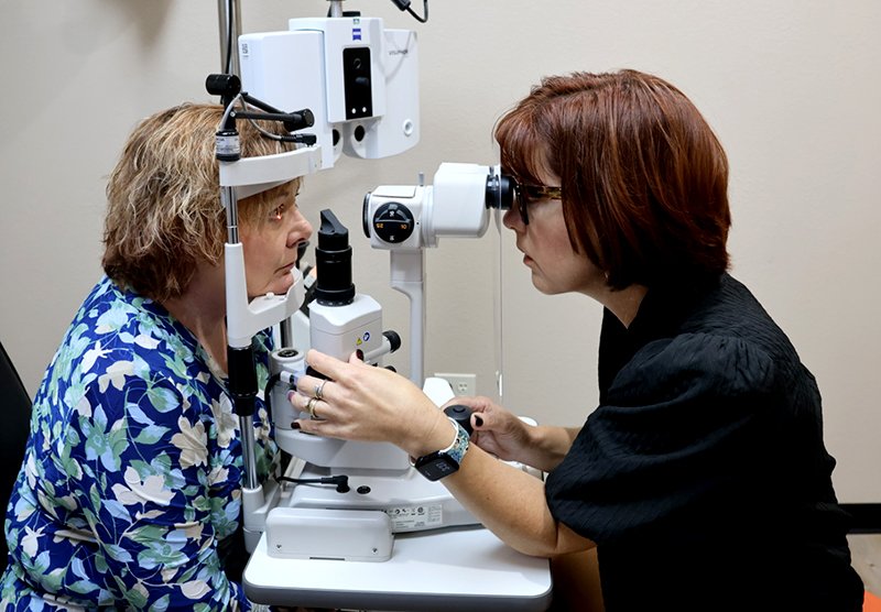 A female optometrist checks a patient's eyes through a machine in an office. 