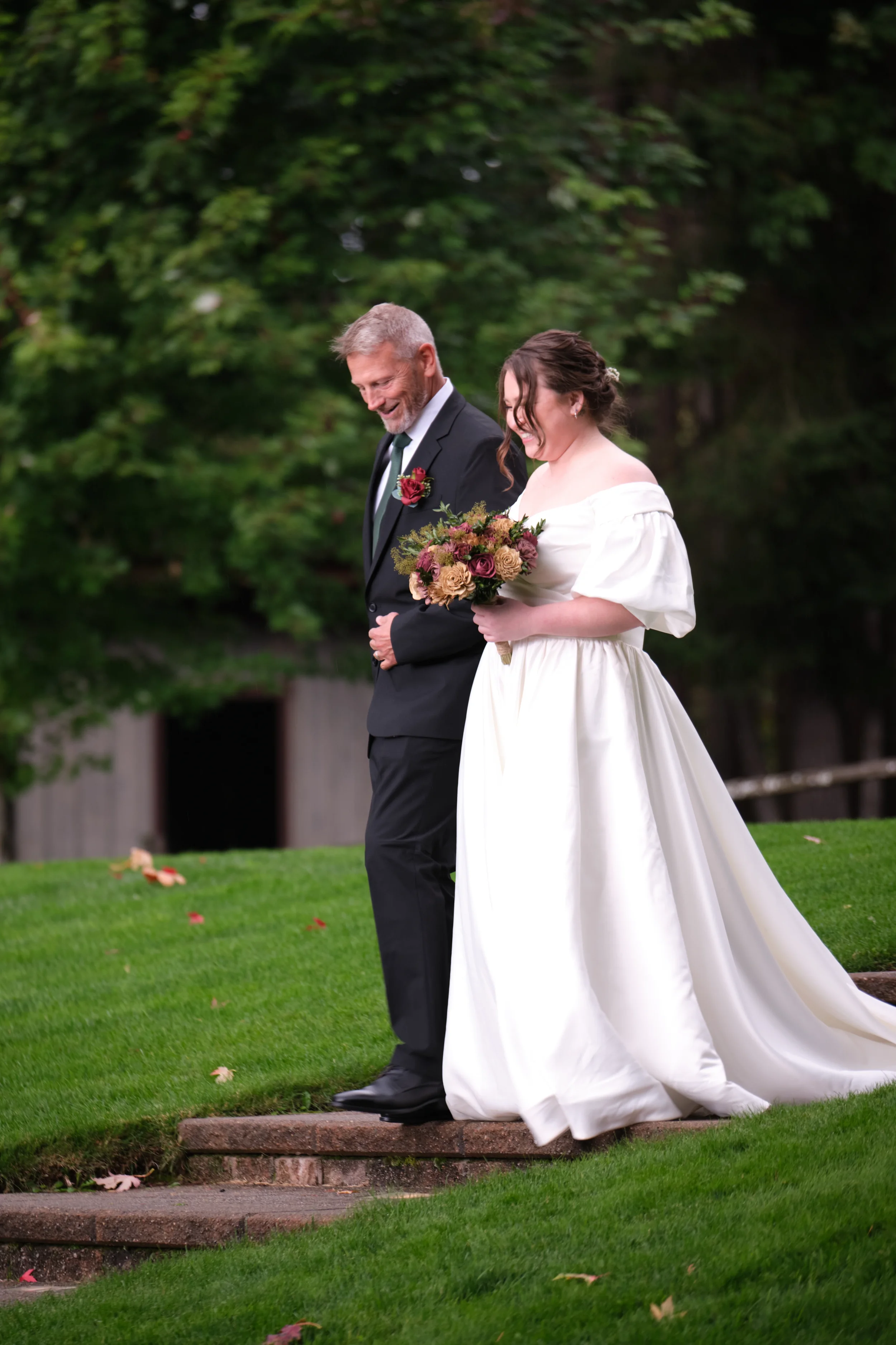 Bride walking outdoors with her father before the wedding ceremony, carrying a colorful bridal bouquet.