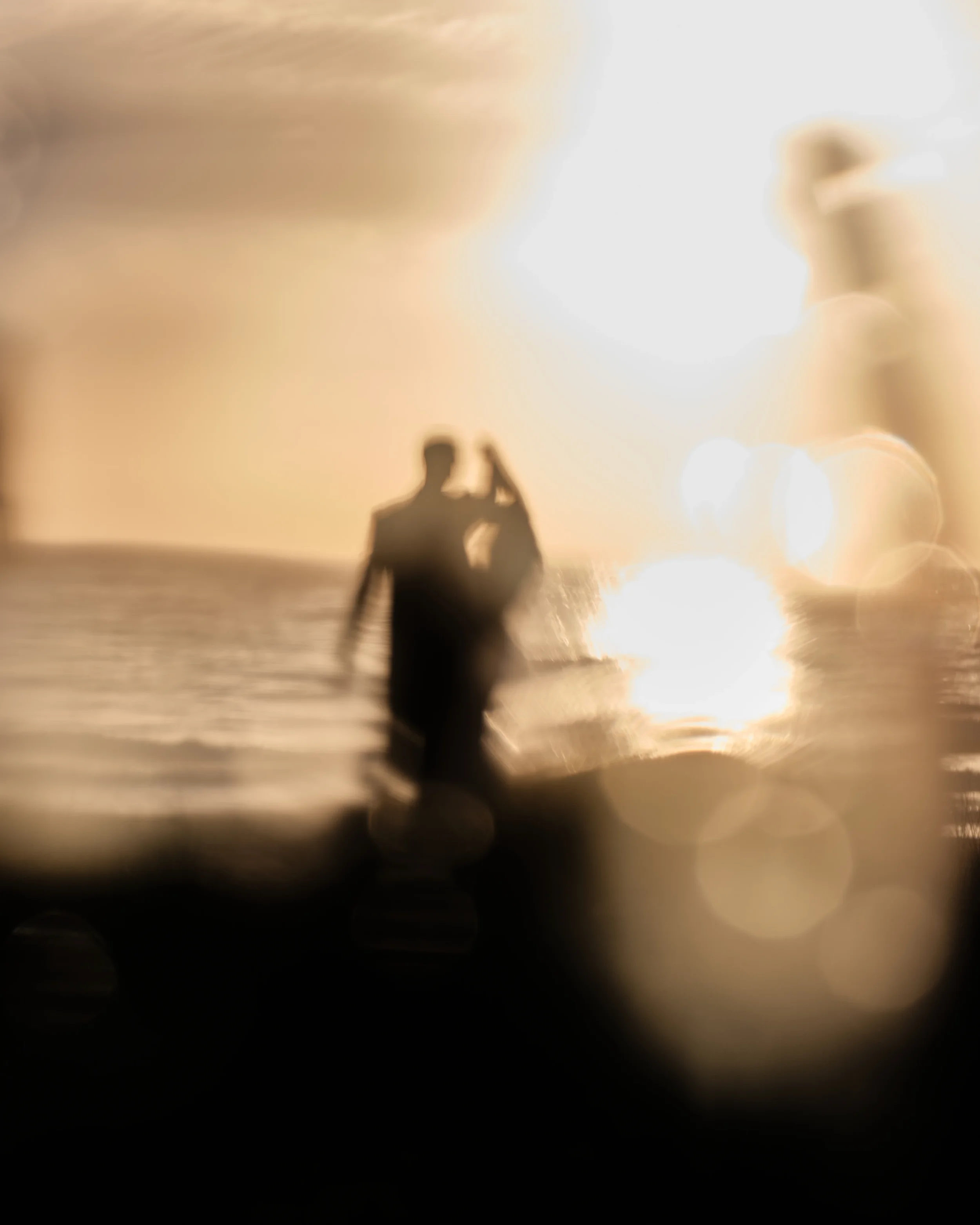 A blurry photo of a person and dog at sunset, with bright sunlight reflecting off a body of water and out-of-focus bokeh lights in the background.