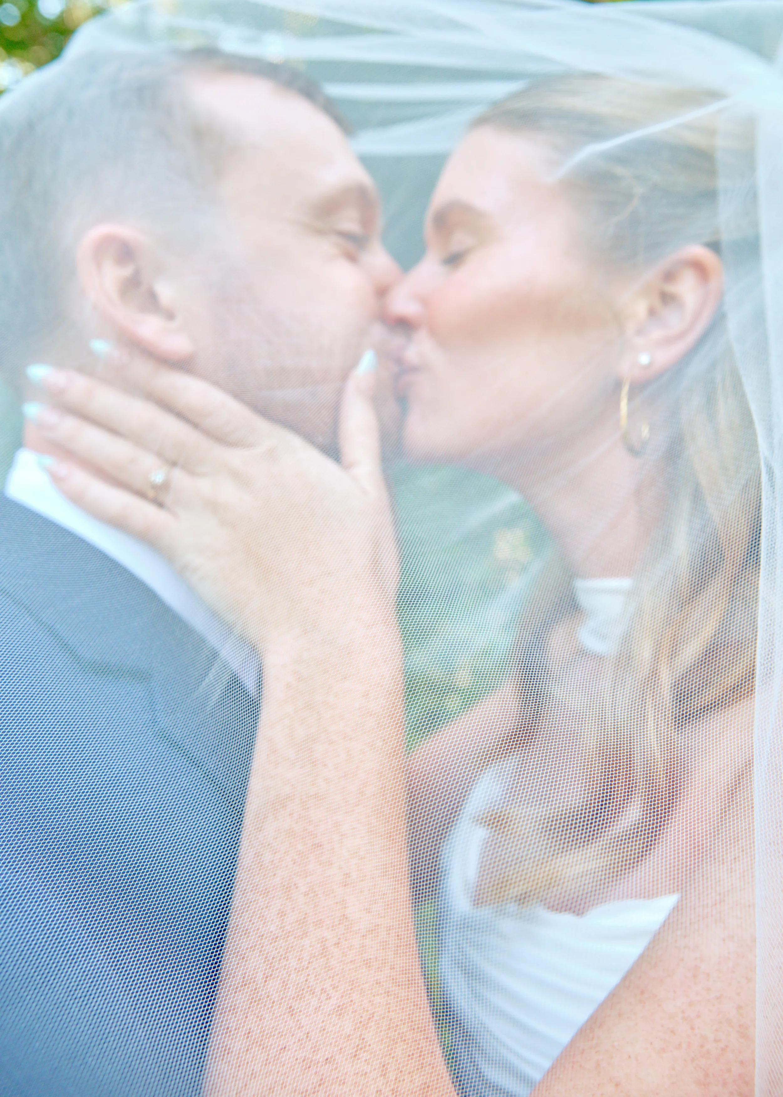 A bride and groom kissing each other behind a window with a mesh screen, with the bride wearing a wedding dress and veil, and the groom in a suit.
