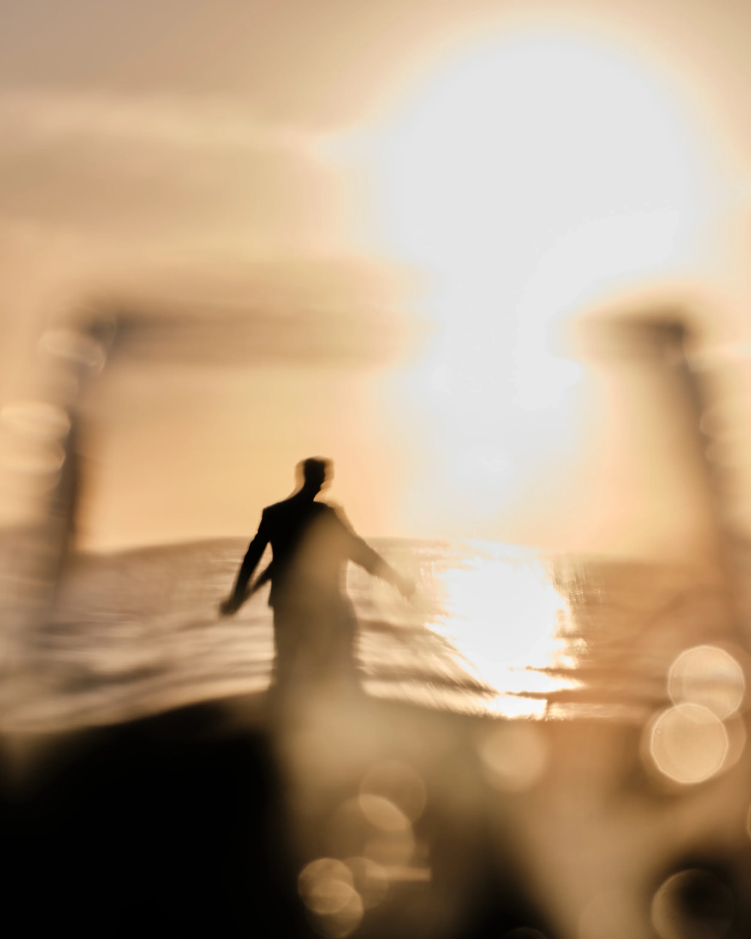 A silhouette of a person riding a bicycle on the beach at sunset, with the sun low on the horizon creating a bright glow in the sky and reflecting on the water.