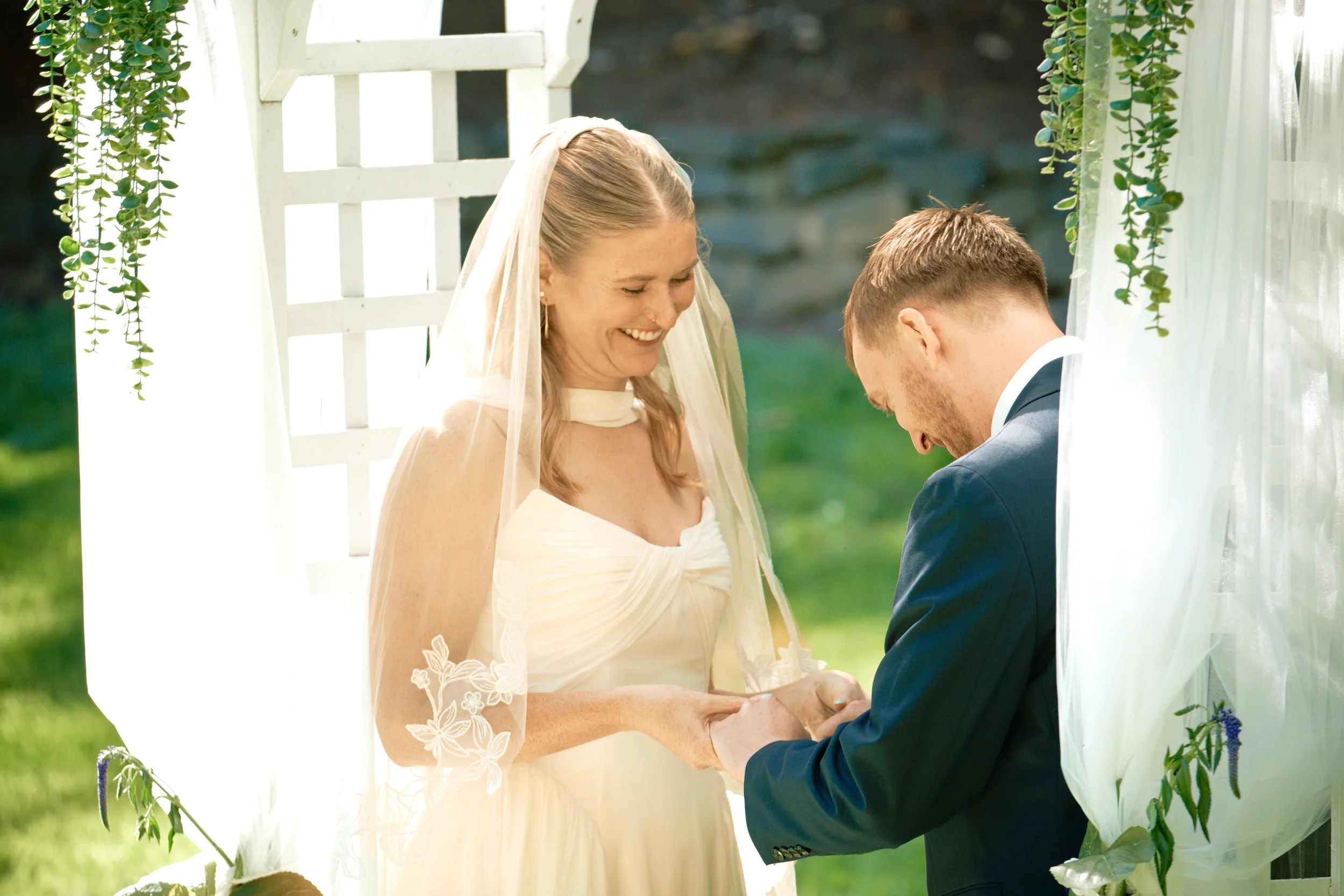 A bride and groom exchanging vows outdoors, holding hands and smiling during their wedding ceremony.