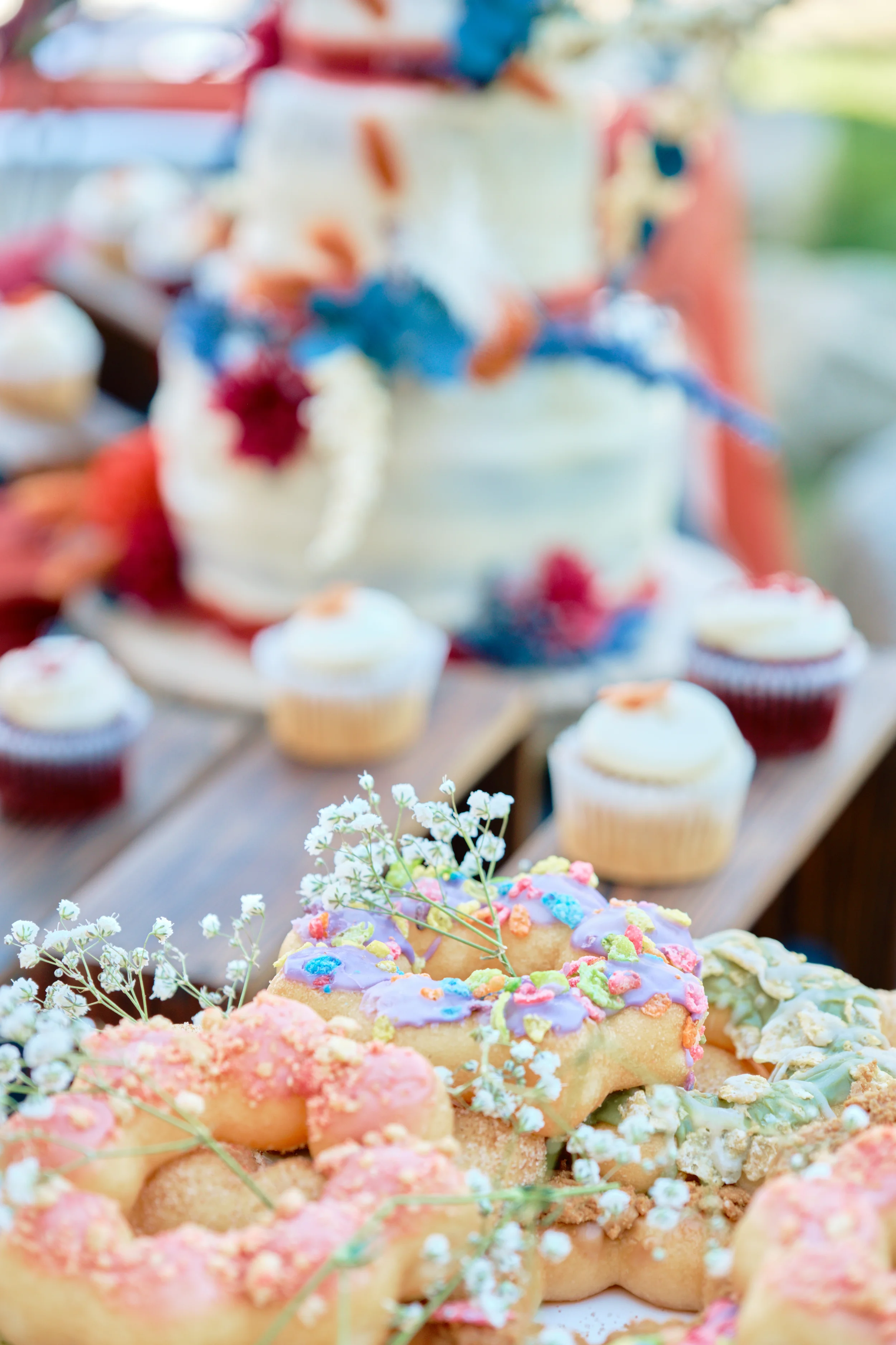 Close-up of a variety of decorated cookies with colorful icing and sprinkles, set on a table with a birthday cake in the background.