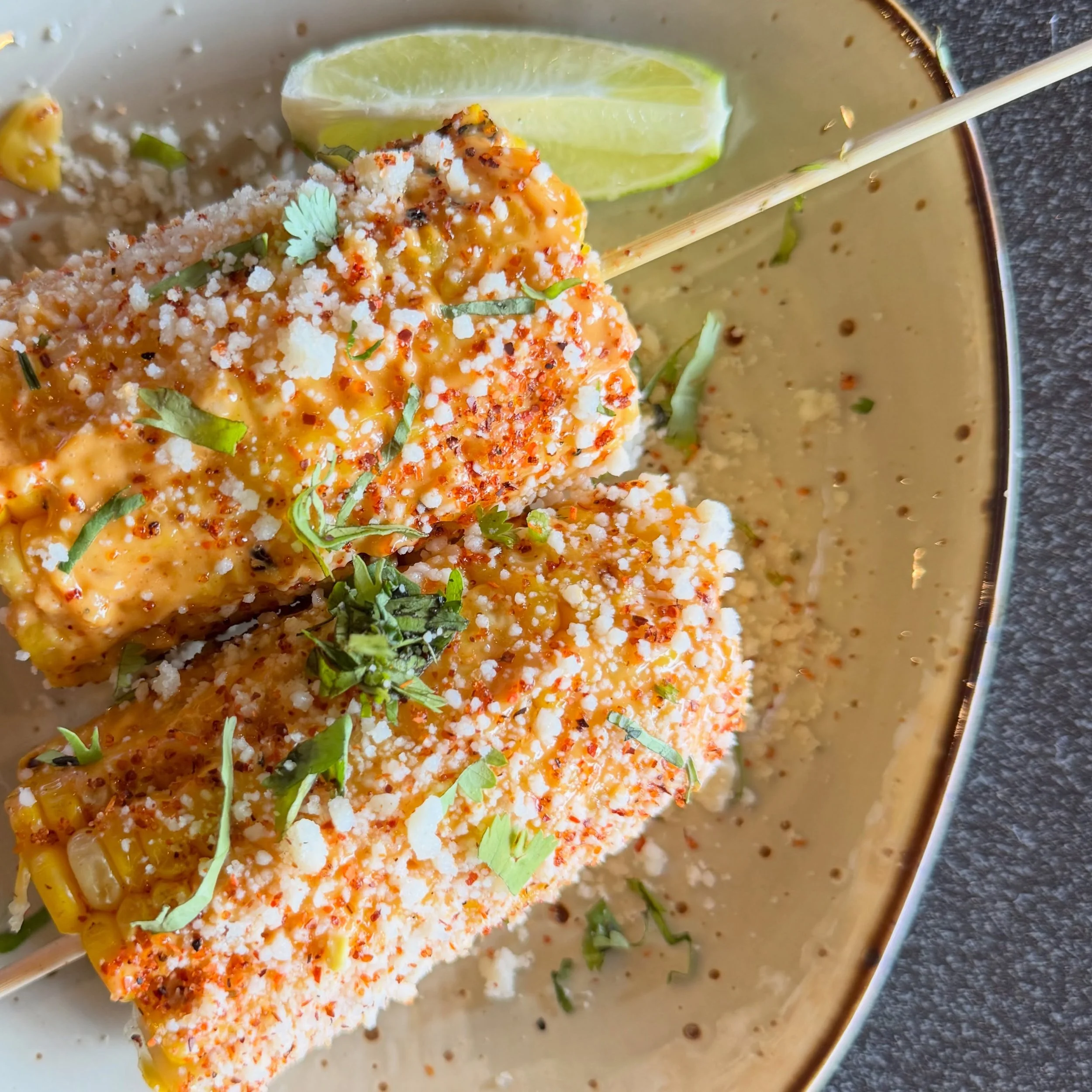 Close-up of a plate with a piece of fish topped with seasonings, garnished with cilantro, and served with lime wedges.