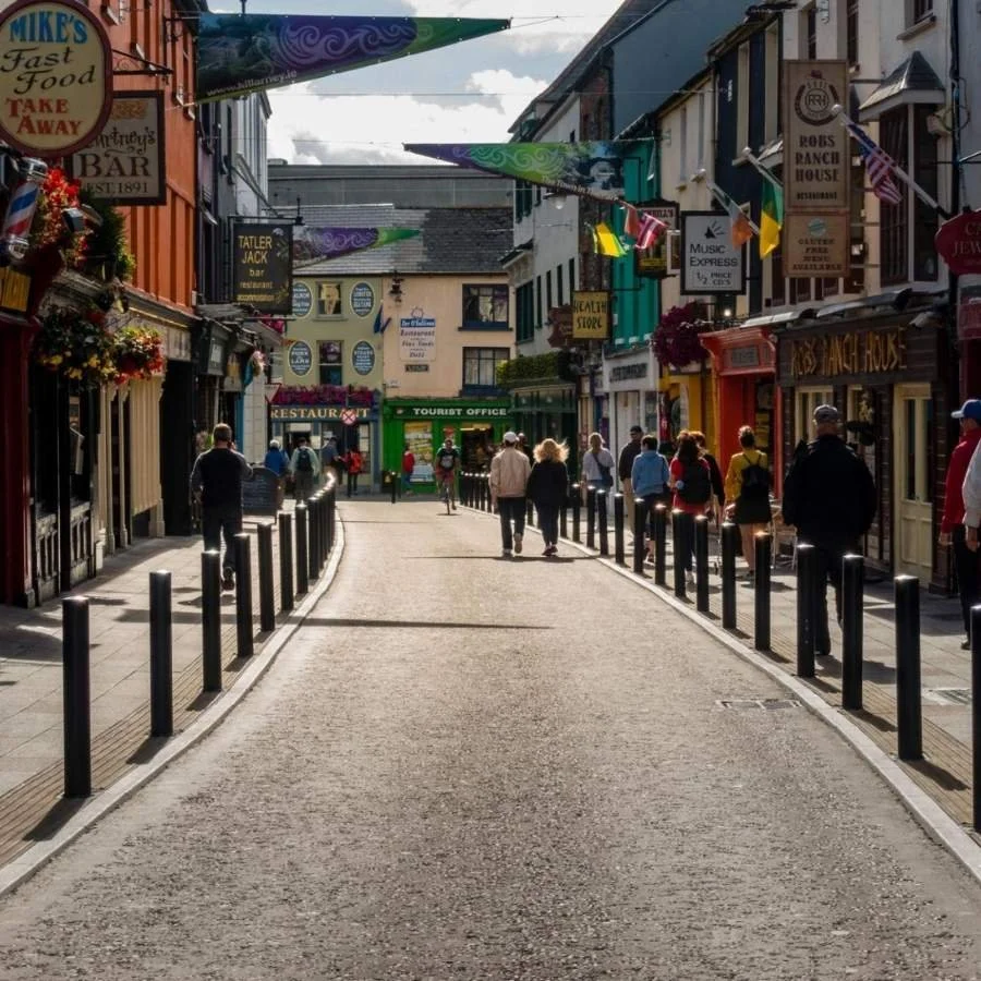 A lively street scene in a tourist area with shops, colorful signs, and pedestrians walking.