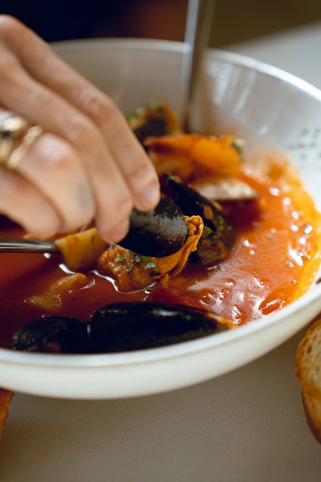 Person scooping mussels from a tomato-based sauce in a white bowl, with a spoon, as part of a seafood dish.