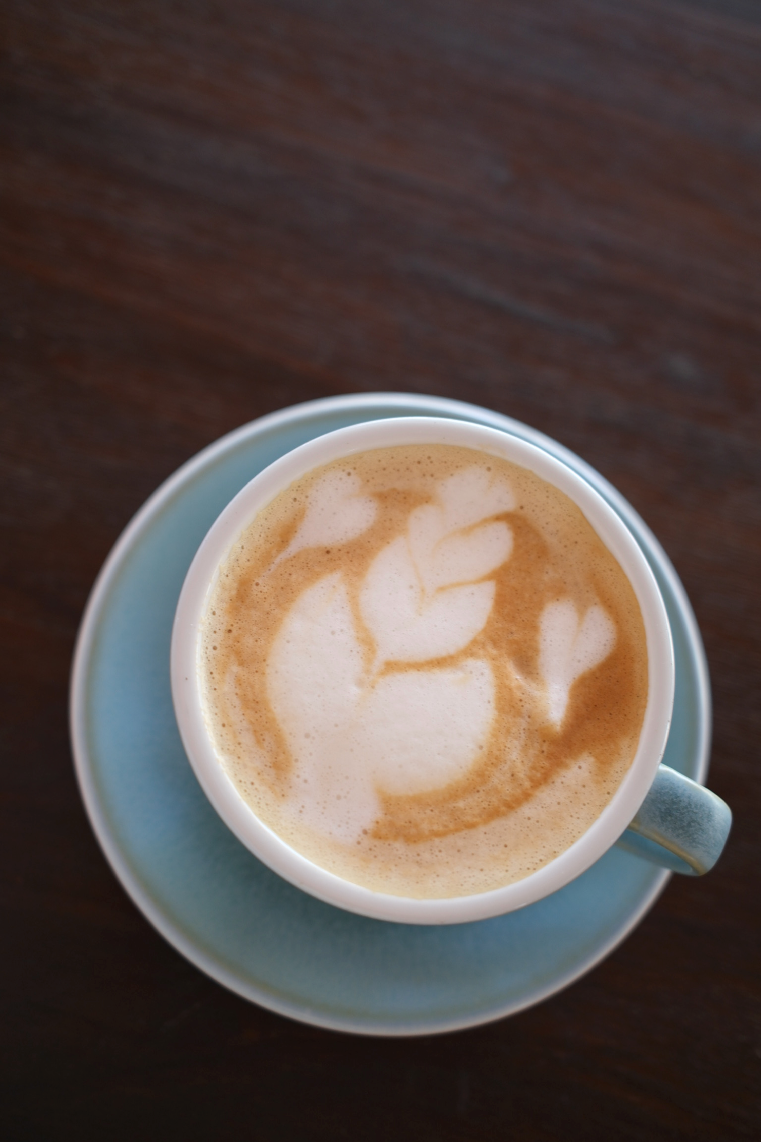 Close-up of a cup of latte with foam art, placed on a matching saucer on a dark wooden table.