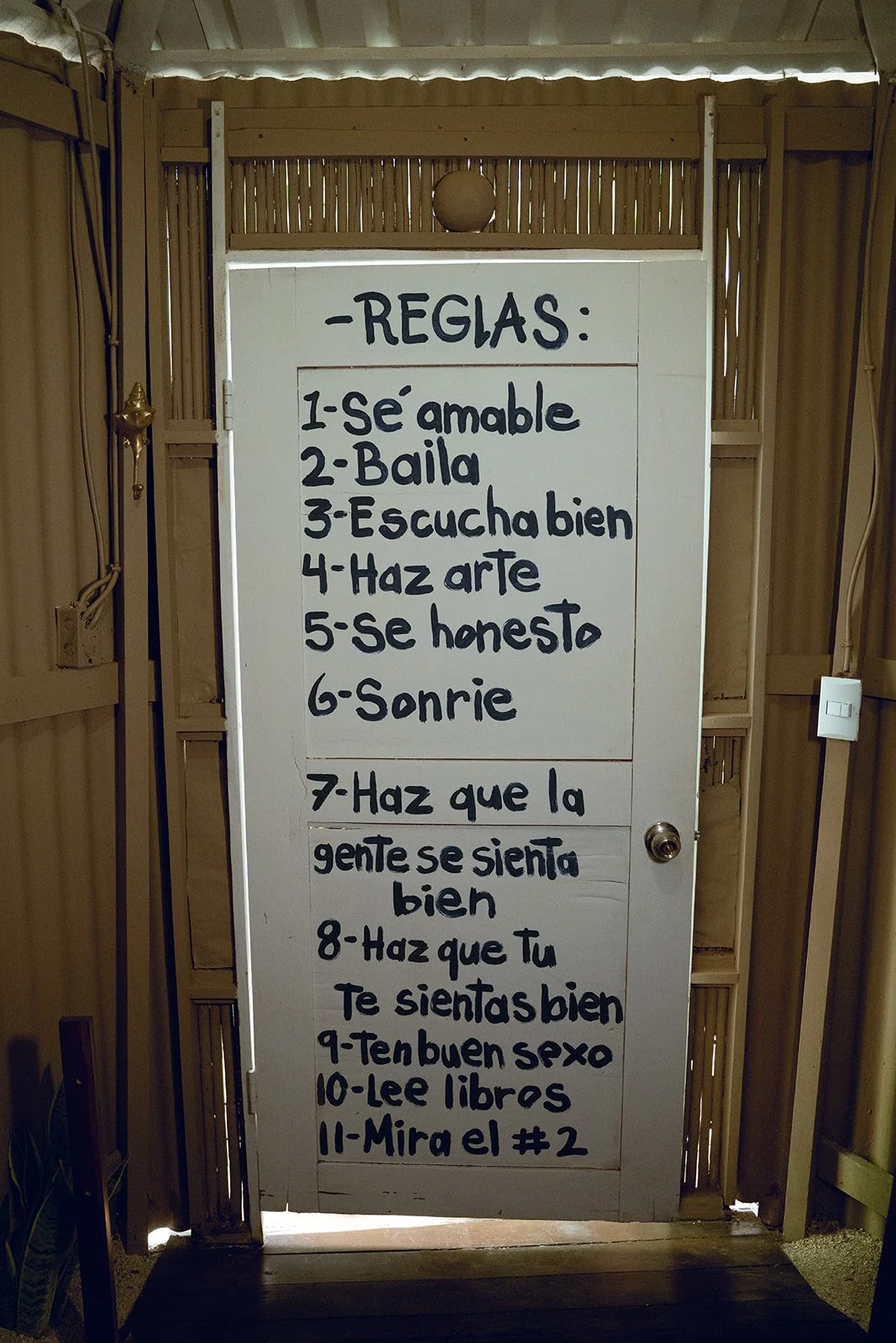 Whiteboard with rules written in Spanish, including being kind, dancing, listening well, making art, being honest, smiling, making people feel good, doing well in bed, reading freely, and checking a specific number.