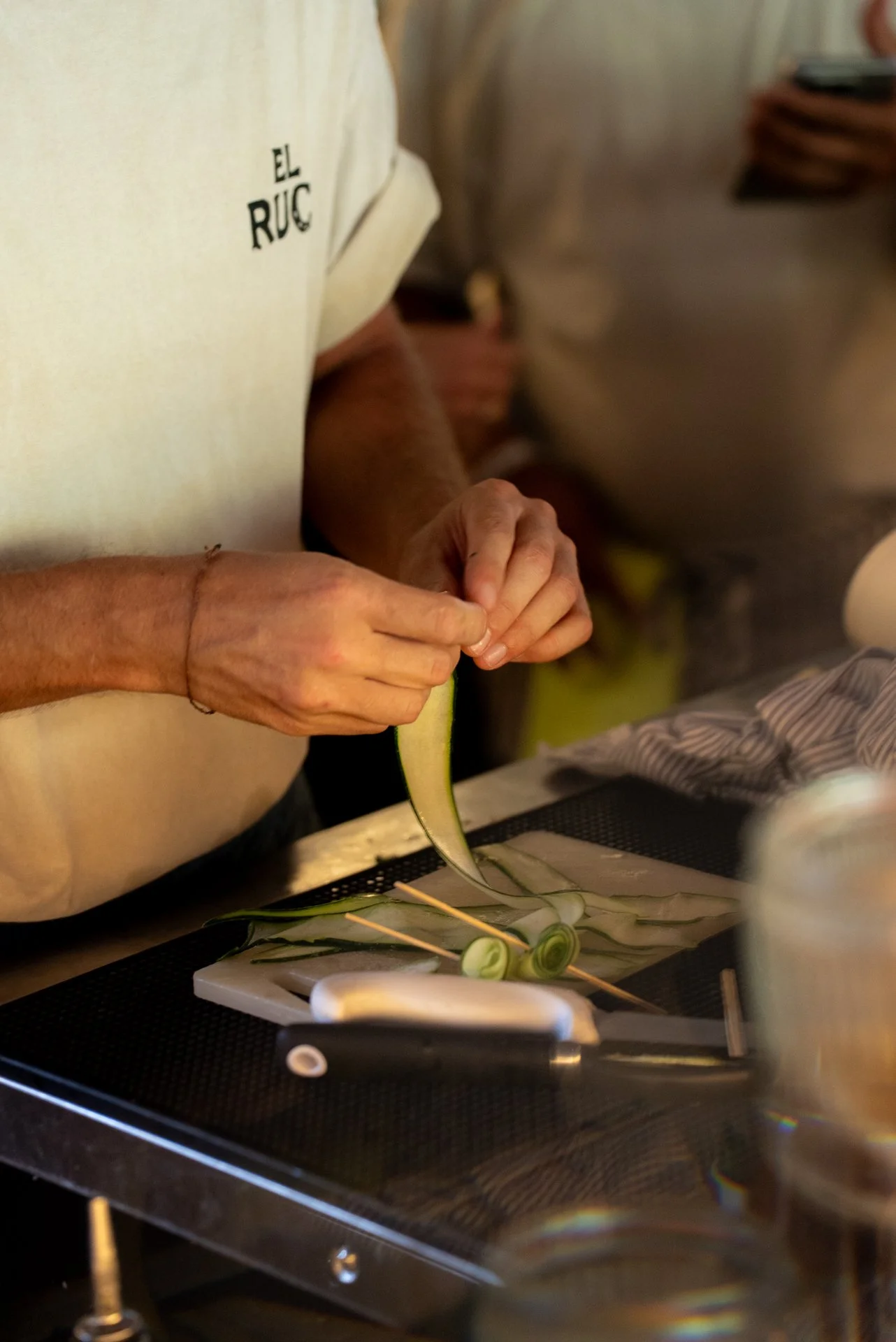 Chef preparing food with sliced zucchini and skewers on a cutting board, in a professional kitchen.