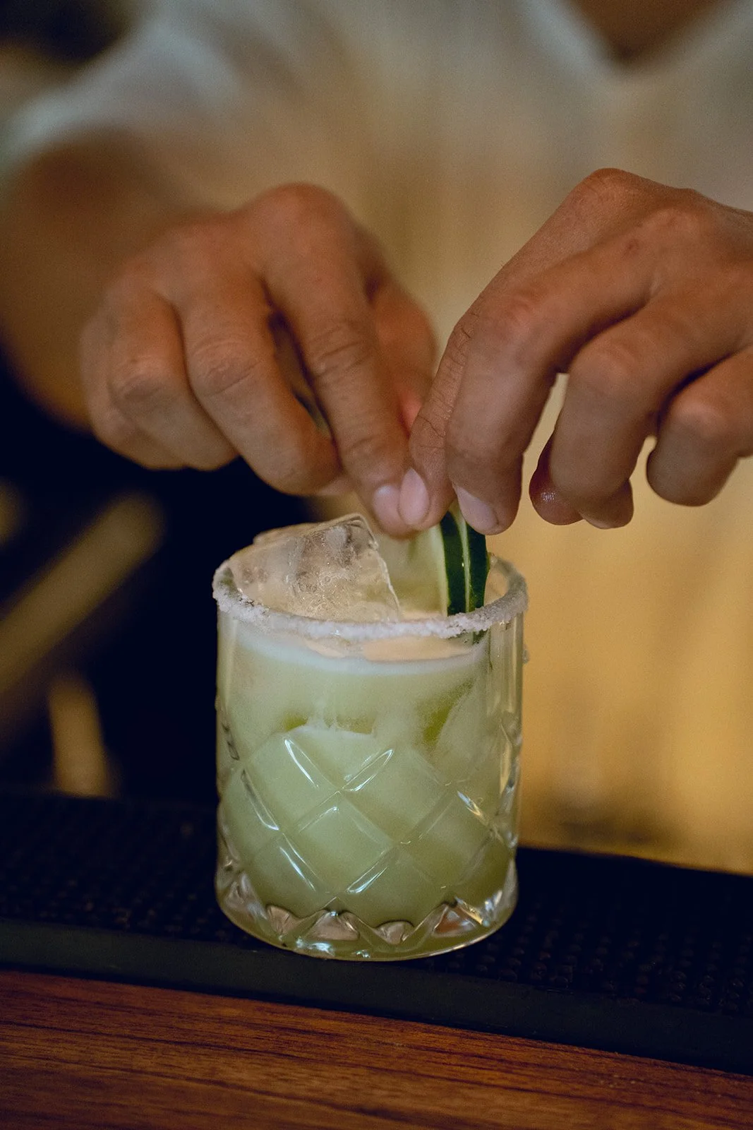 Close-up of hands preparing a cocktail with lime and ice in a decorative glass.