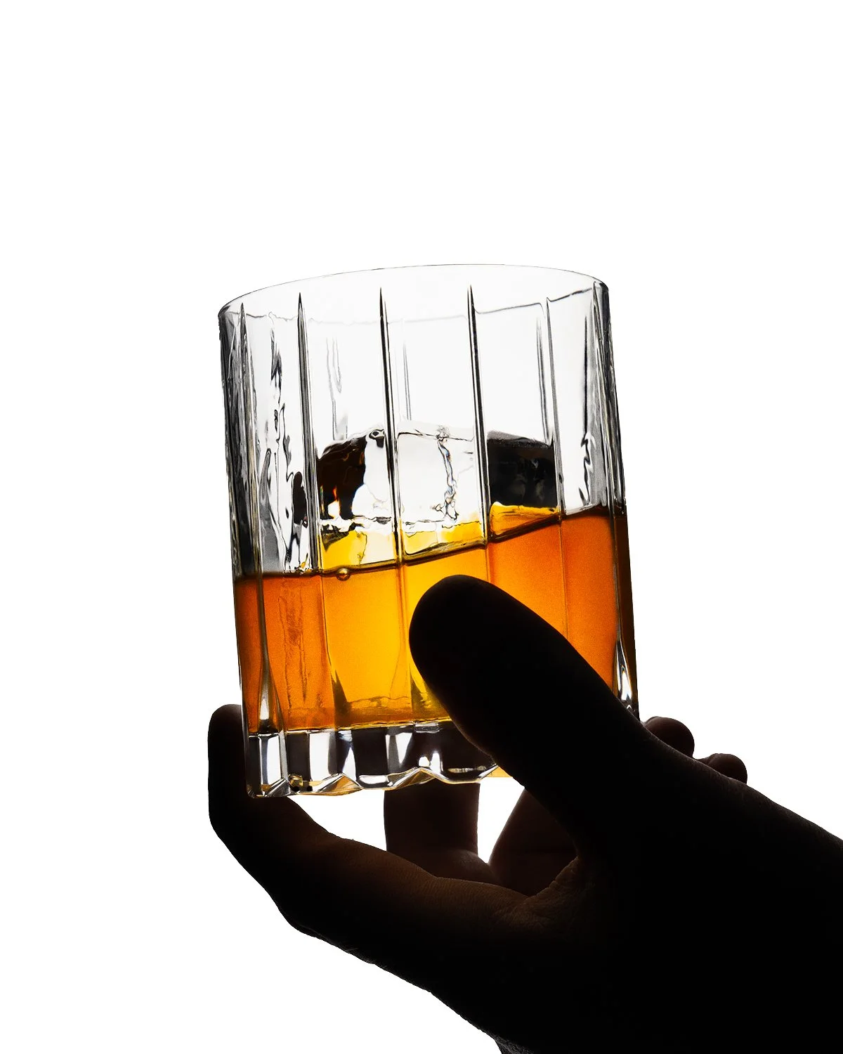 A hand holding a glass of amber-colored liquor against a white background.