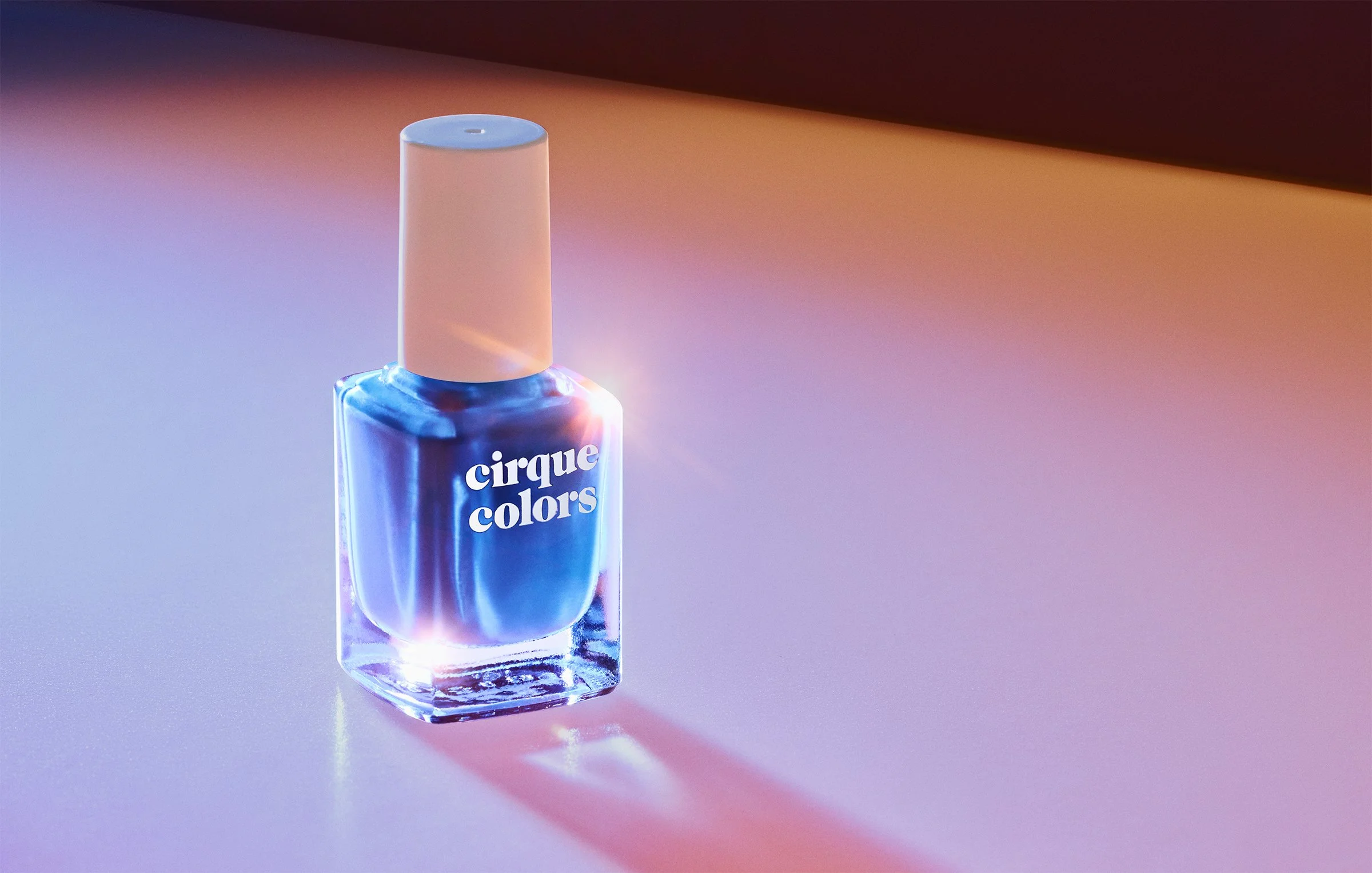 Colorful nail polish bottle with pink cap on a reflective surface, emitting colorful light reflections.