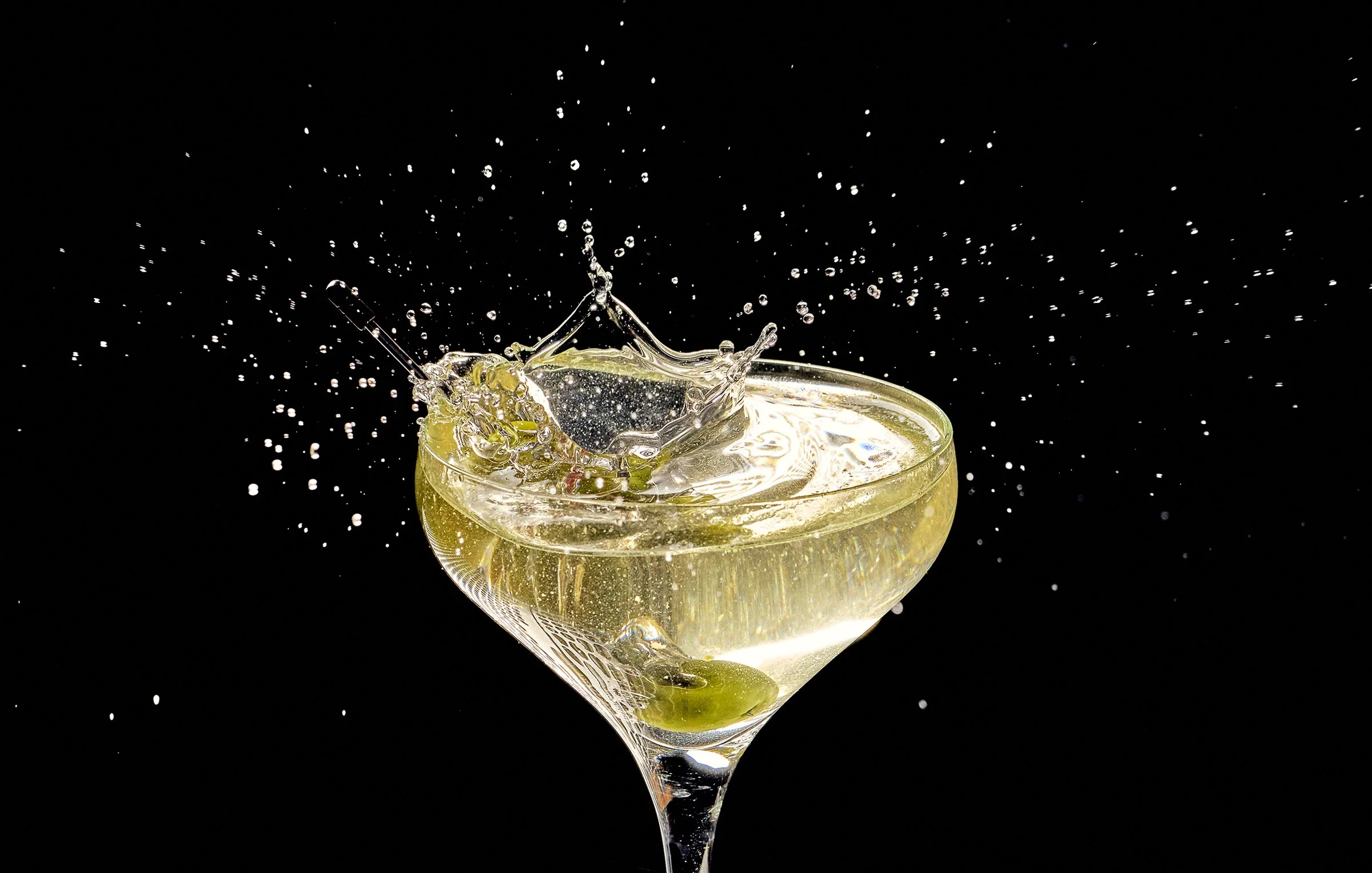 A close-up of a champagne glass filled with sparkling wine, with the liquid splash frozen in mid-air against a black background.