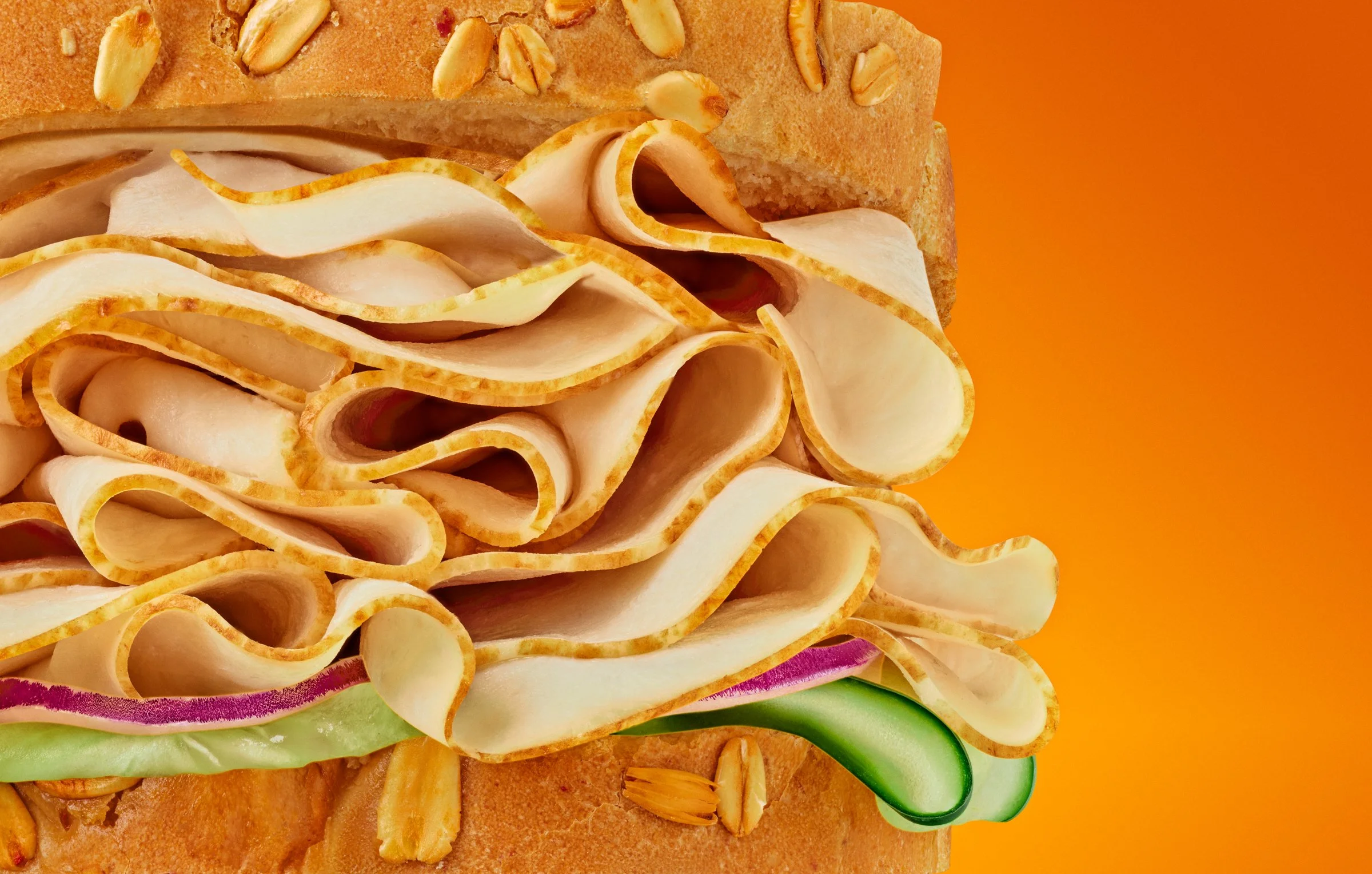 Close-up of a sandwich with layers of cheese, lettuce, red onion, and turkey on a bread bun, garnished with almond slices.