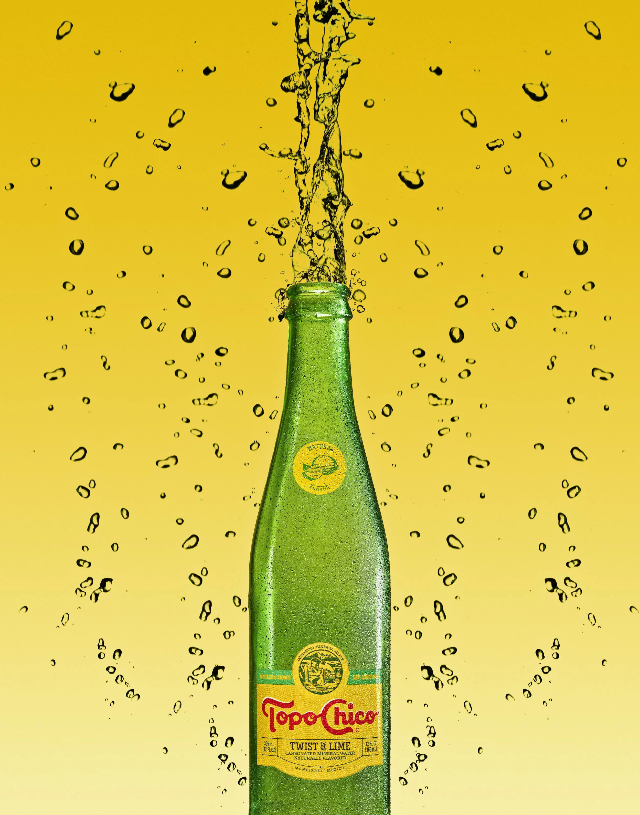 A green glass bottle of Topo Chico Twist of Lime mineral water with bubbles, against a yellow background with splash effects.