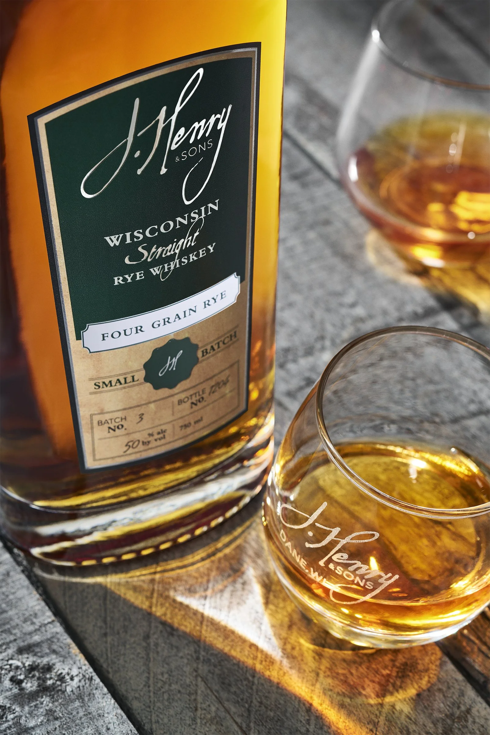 A bottle of J. Henny & Sons Wisconsin Straight Rye Whiskey and a glass of whiskey on a wooden surface.