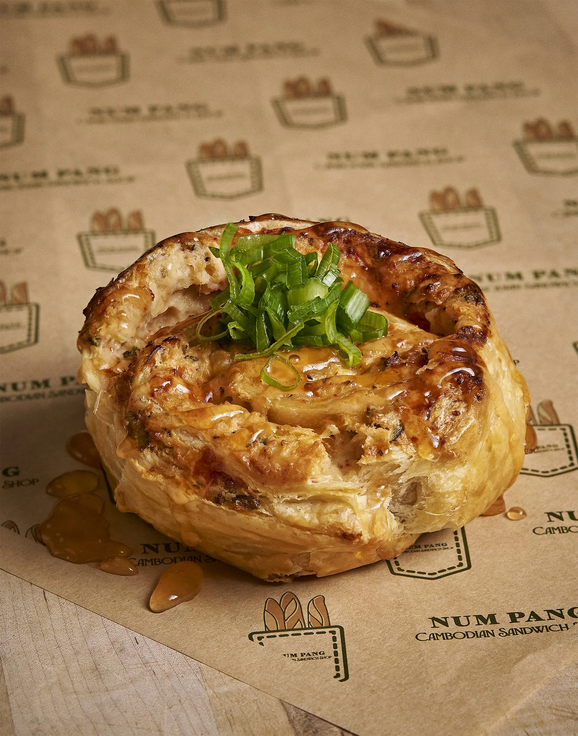 Close-up of a Cambodian sandwich with chopped green onions on top, resting on branded paper.