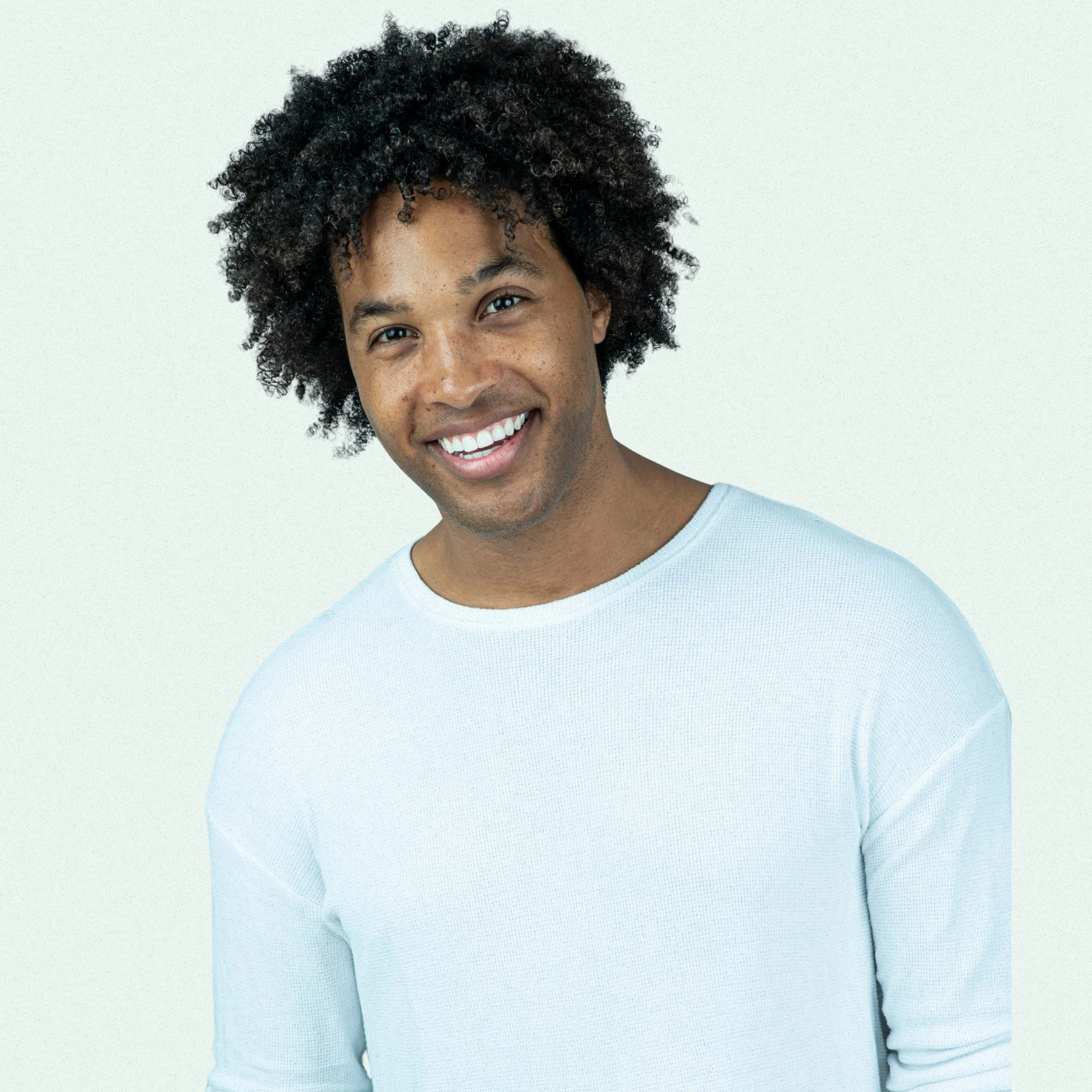 Close-up of a smiling young man with curly hair wearing a light blue shirt against a plain white background and is a photo of Oren Williamson